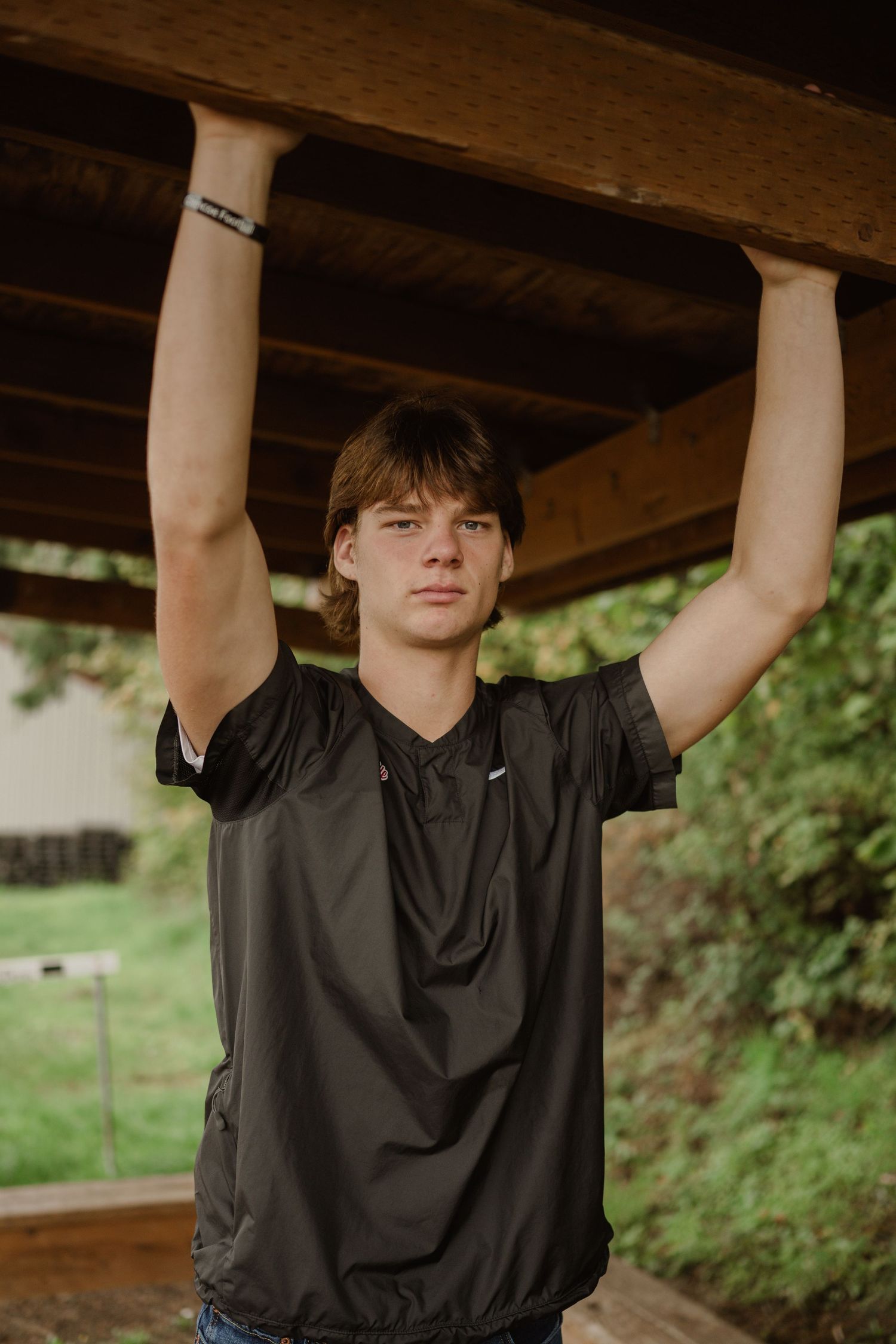 Athletic person wearing black shirt exercising under wooden beams at an outdoor shelter.