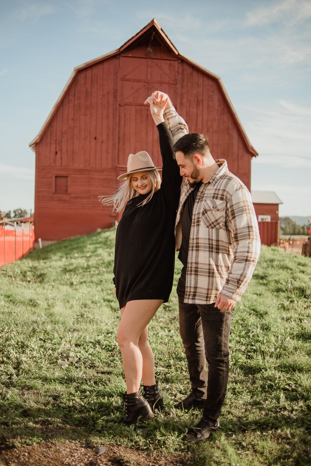 A couple dancing and laughing in front of a classic red barn on a sunny day.