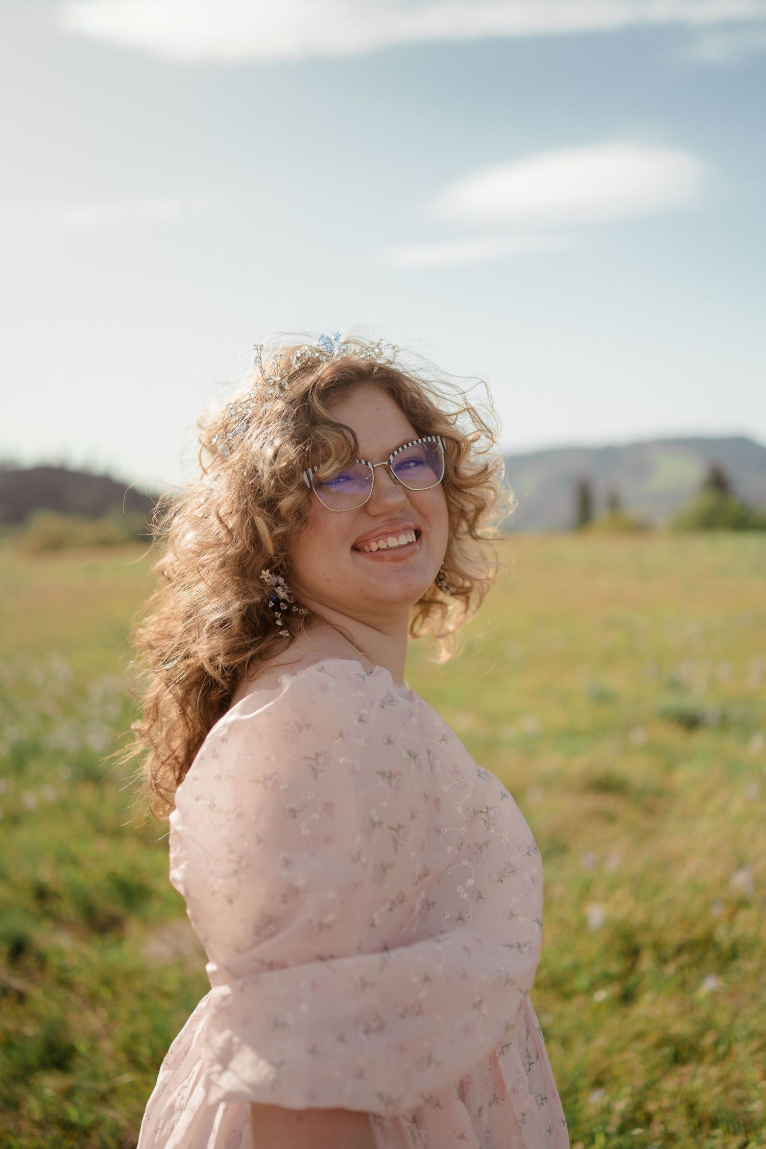 Portrait in pink dress standing in sunny meadow with mountains in background.