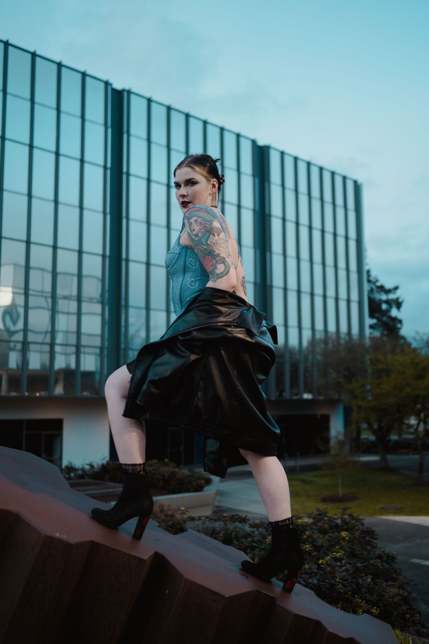 Person in alternative fashion poses on concrete structure near glass office building.