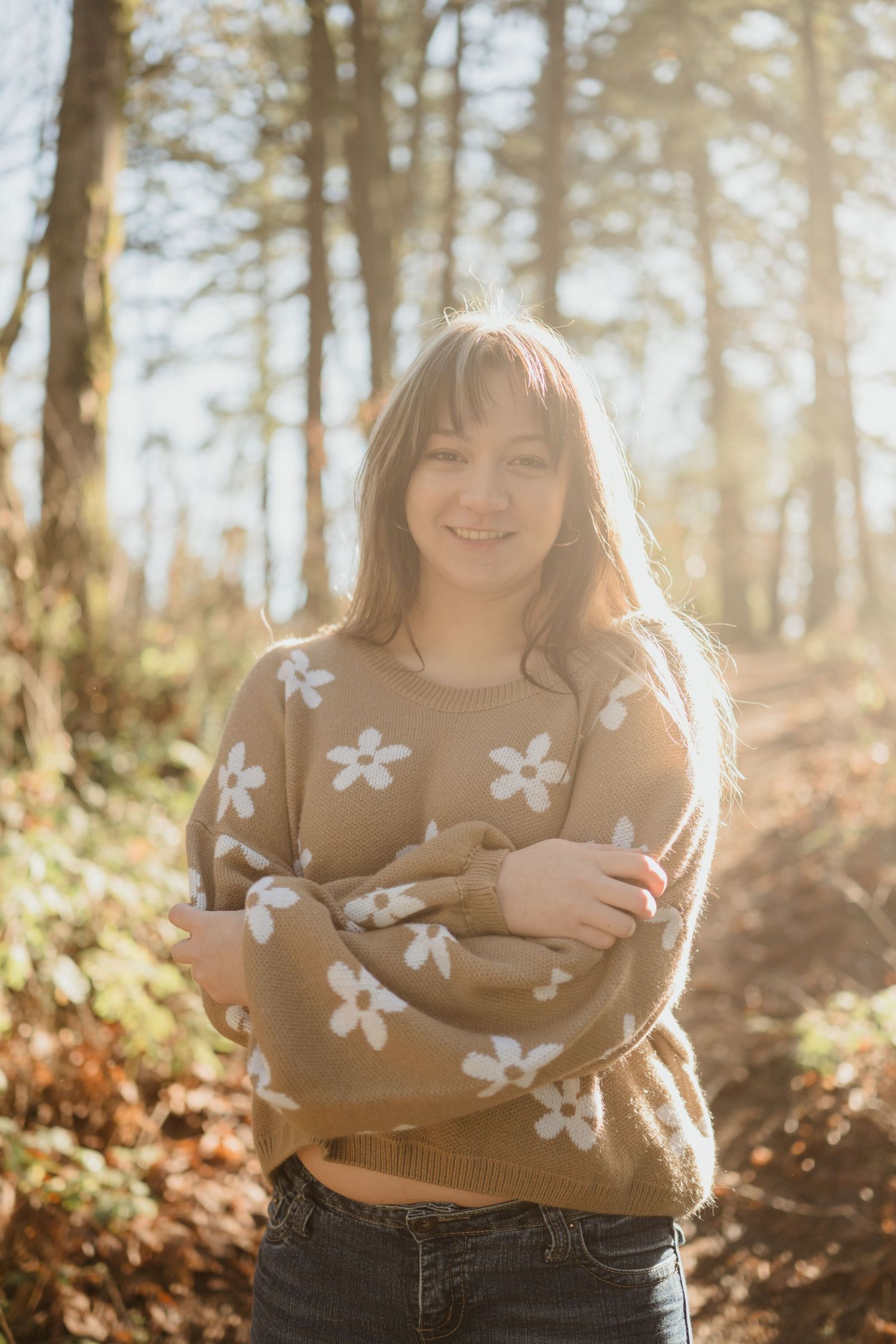 Person wearing floral sweater hugging themselves in sunny autumn forest.