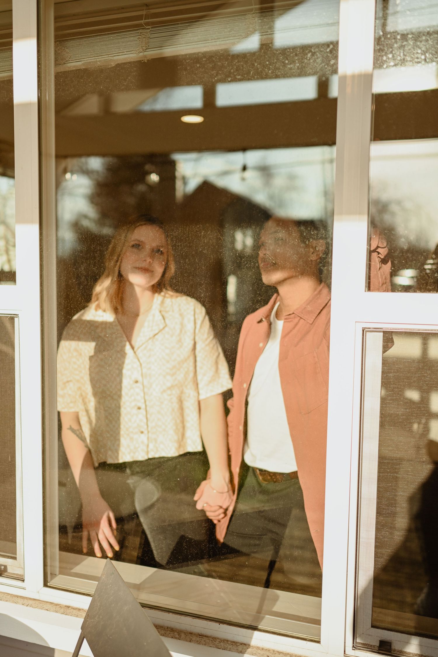 A sun-filled window frame capturing a couple holding hands in vintage-style lighting.