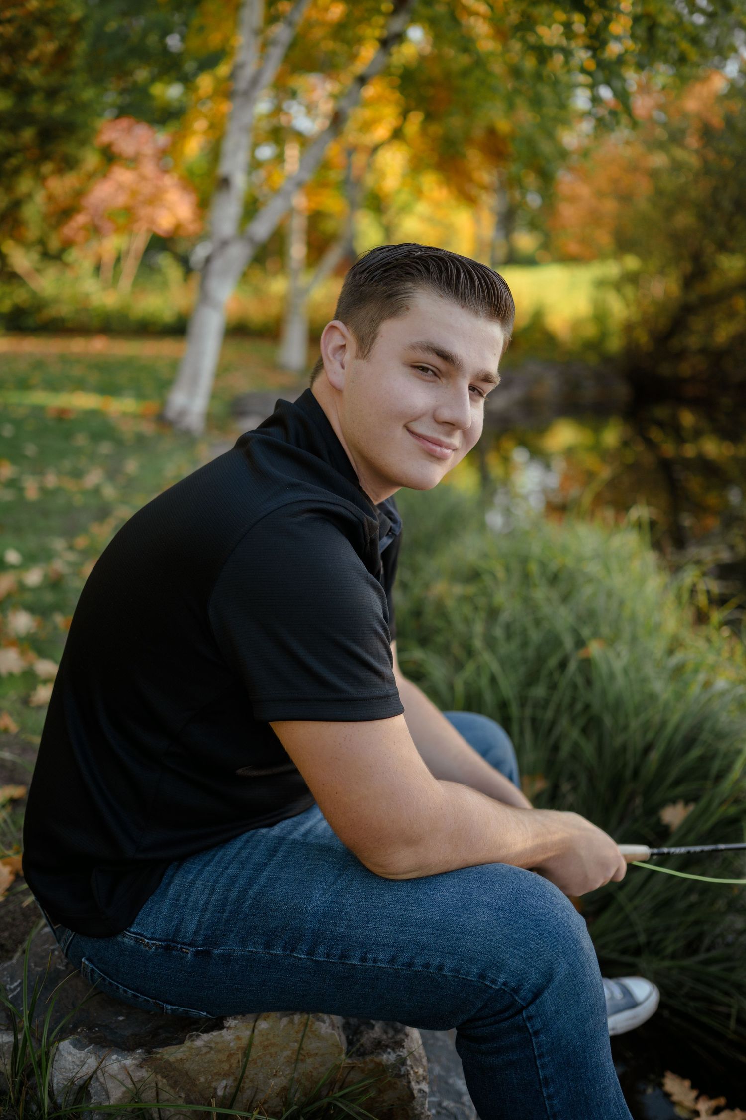 Person sitting on log during autumn with trees and fall foliage in background.