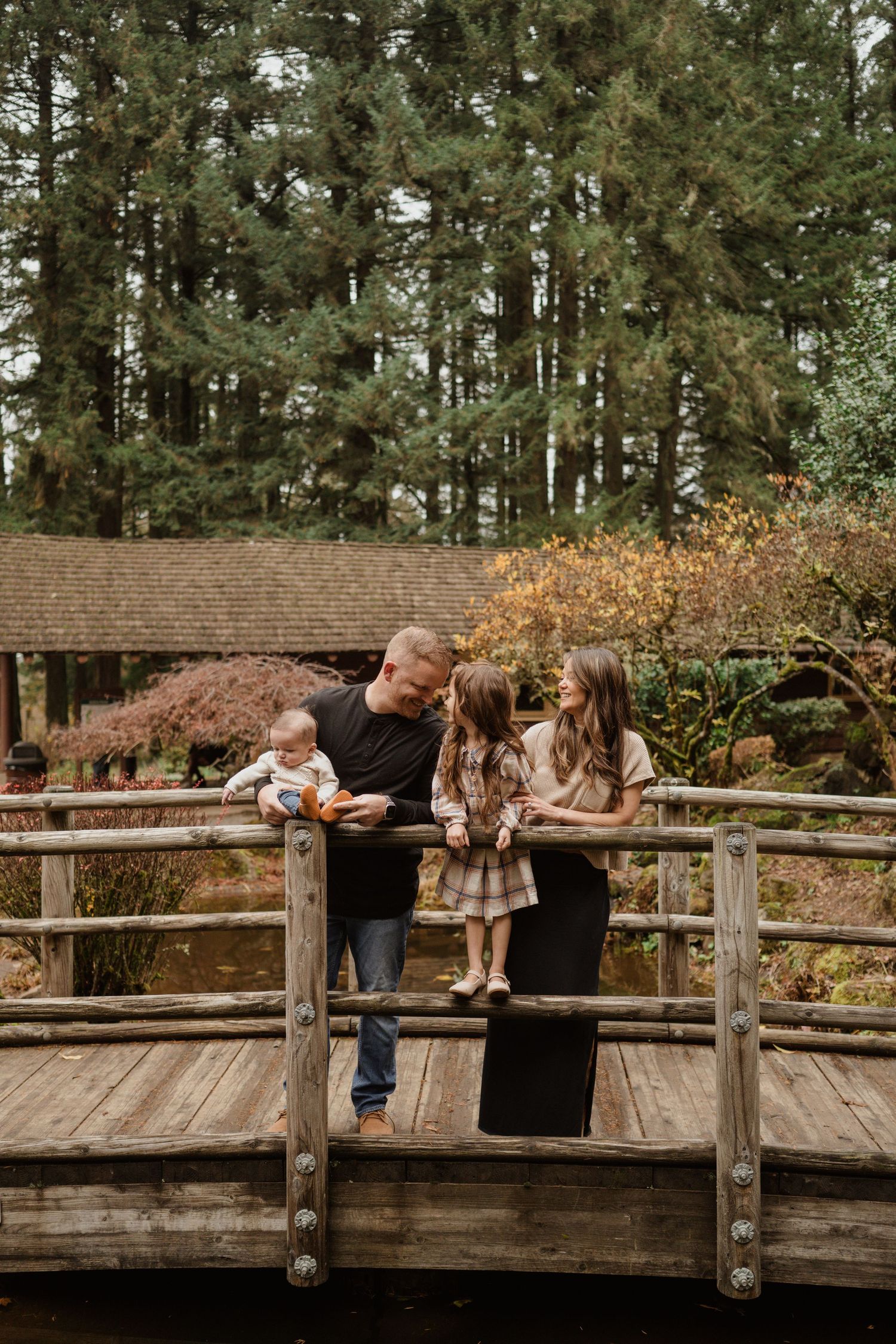 Family standing together on a wooden bridge in a forest park during autumn.