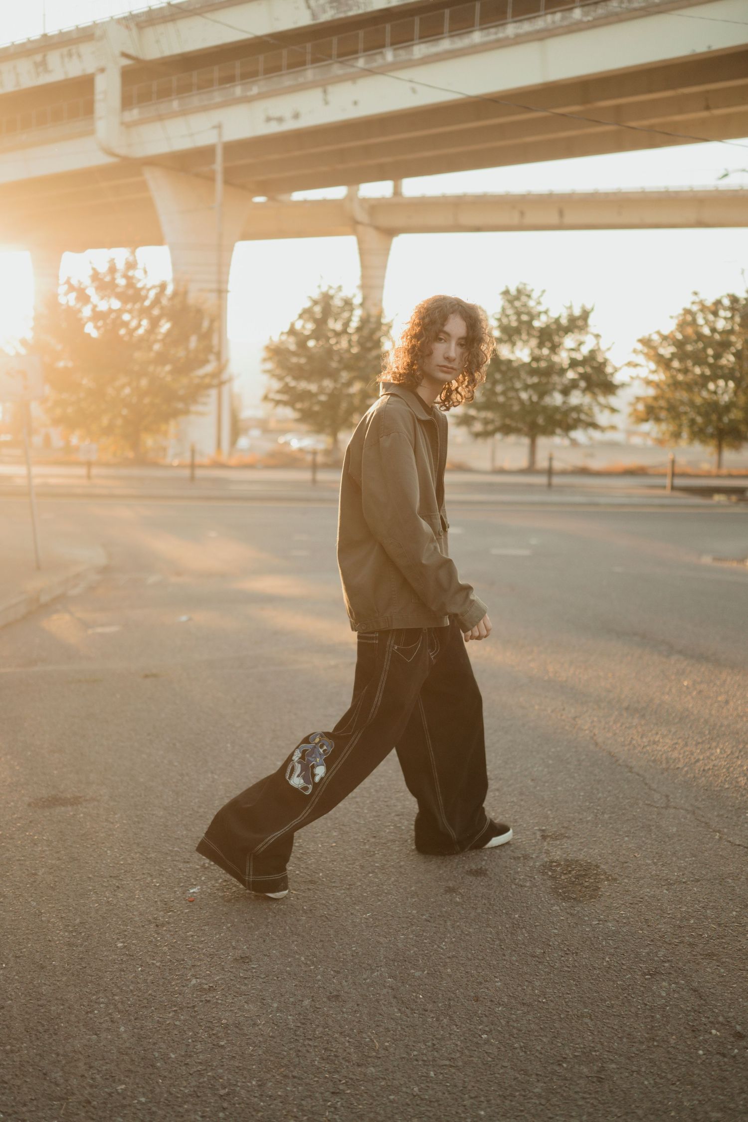 A person walking at sunset under a highway overpass with golden light.