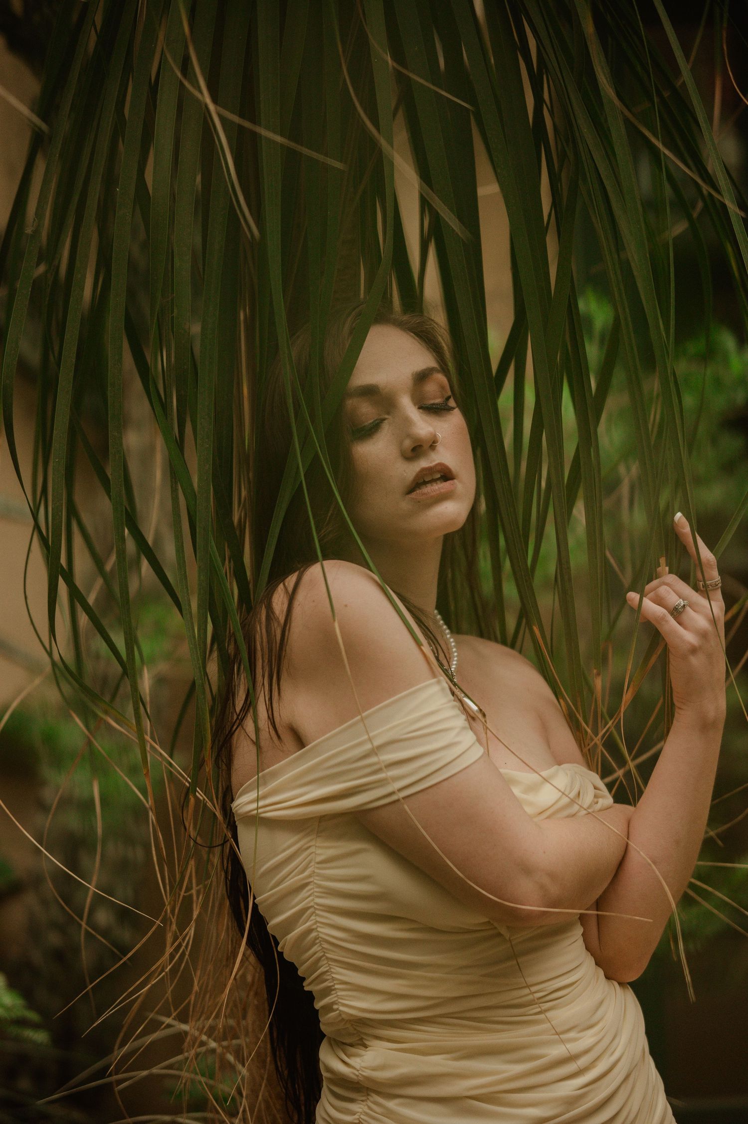 A dreamy portrait in a cream dress among hanging vines and tropical foliage with moody natural lighting.
