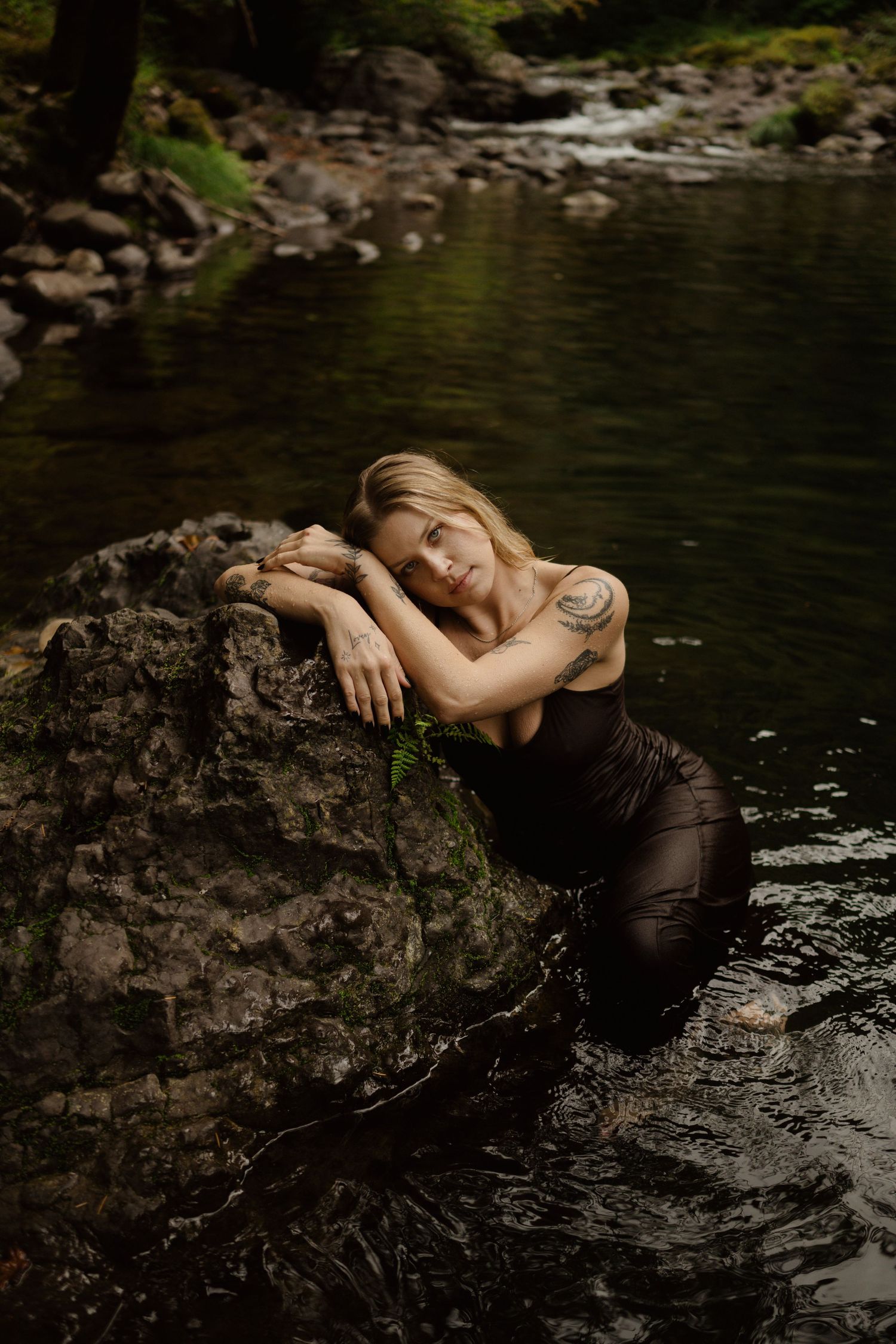Dreamy water portrait leaning against rock in dark forest stream.