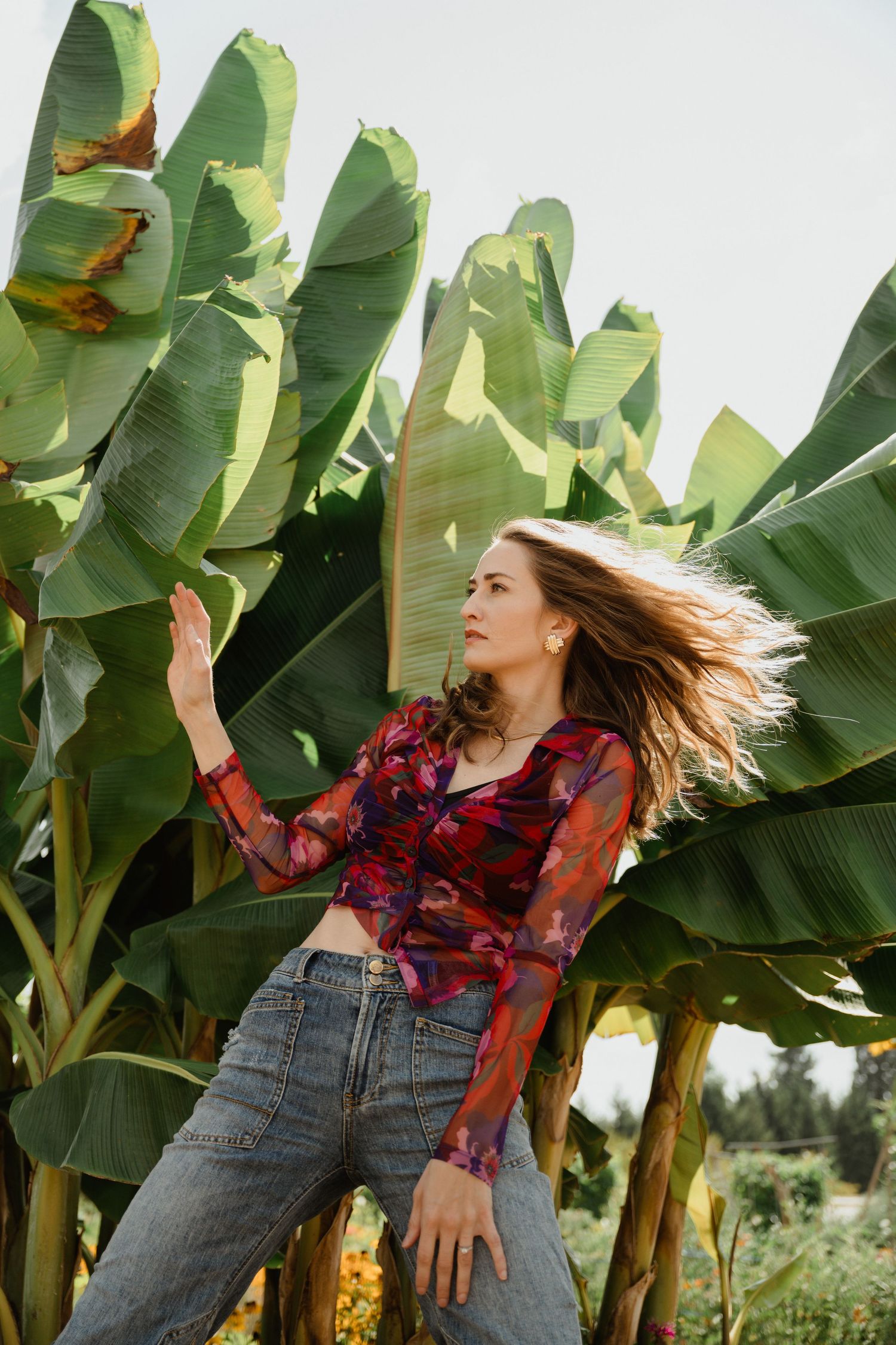 Dynamic fashion pose with flowing hair against tropical banana leaves.