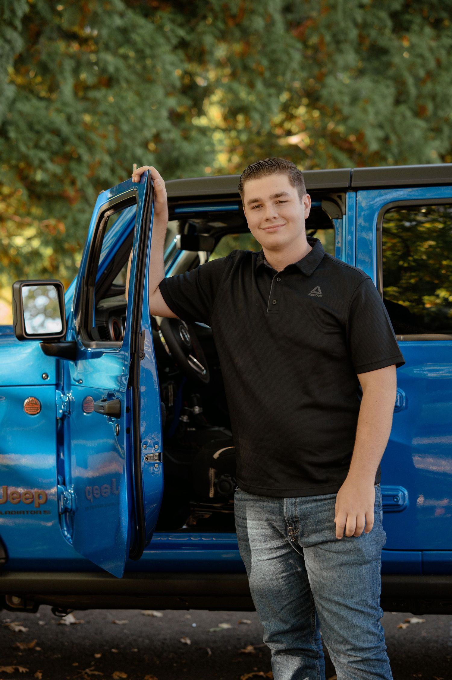 Person standing next to vintage blue truck with door open in autumn setting.