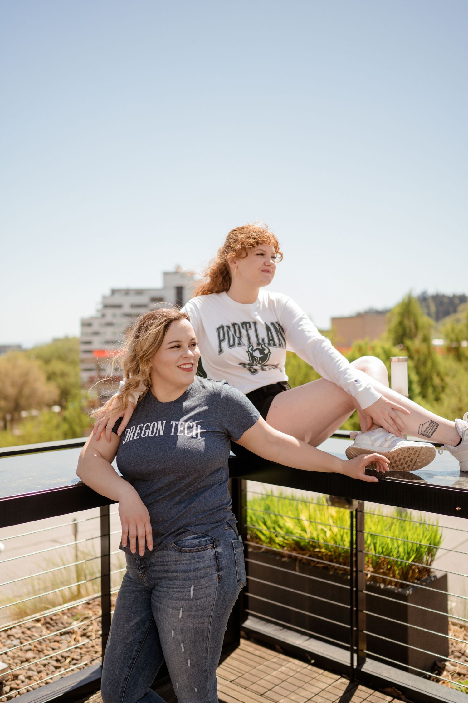 Friends in college t-shirts pose casually on sunny outdoor terrace.