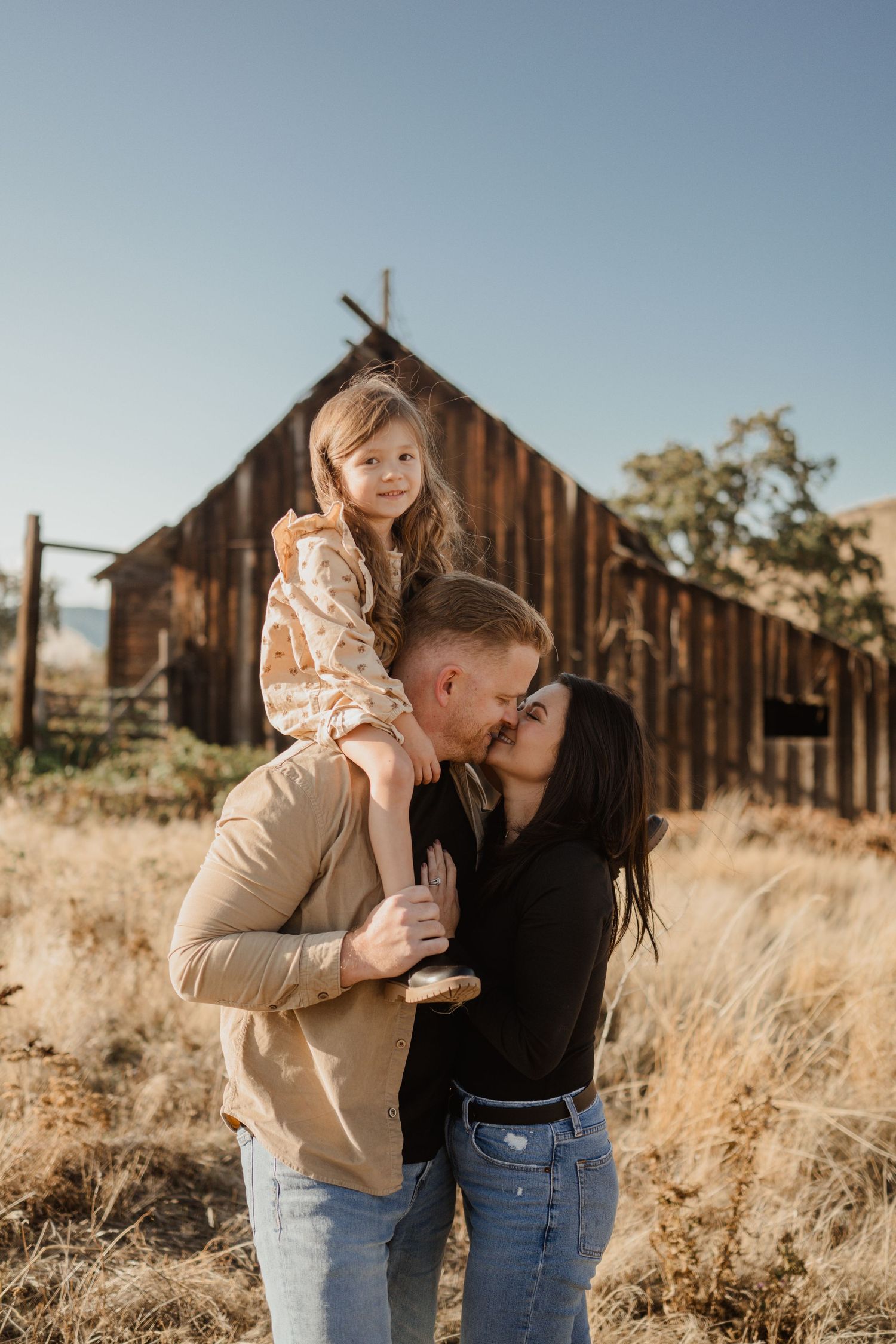 Intimate family portrait in front of rustic wooden barn during golden hour.