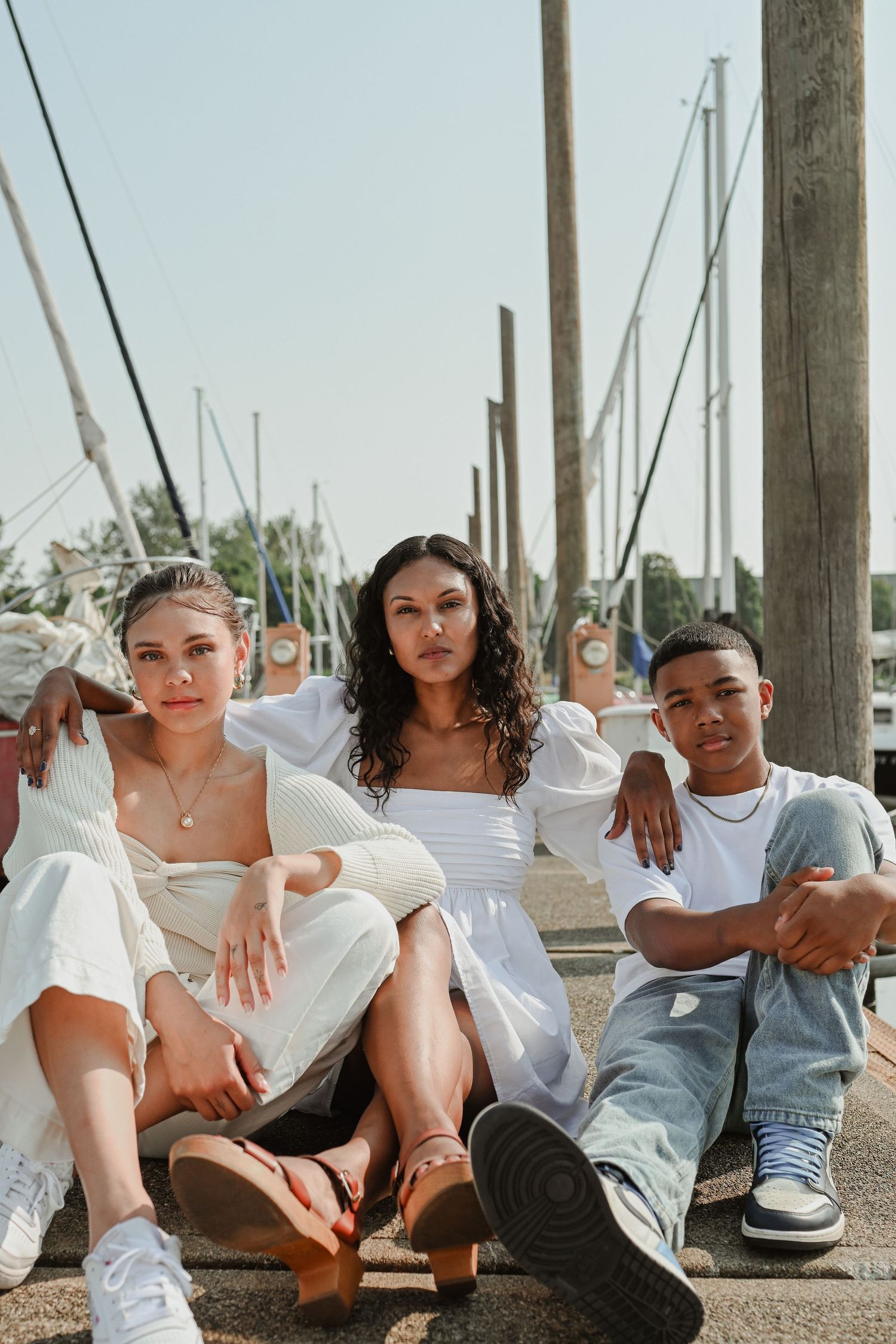 Three friends in casual attire sitting together on marina steps.