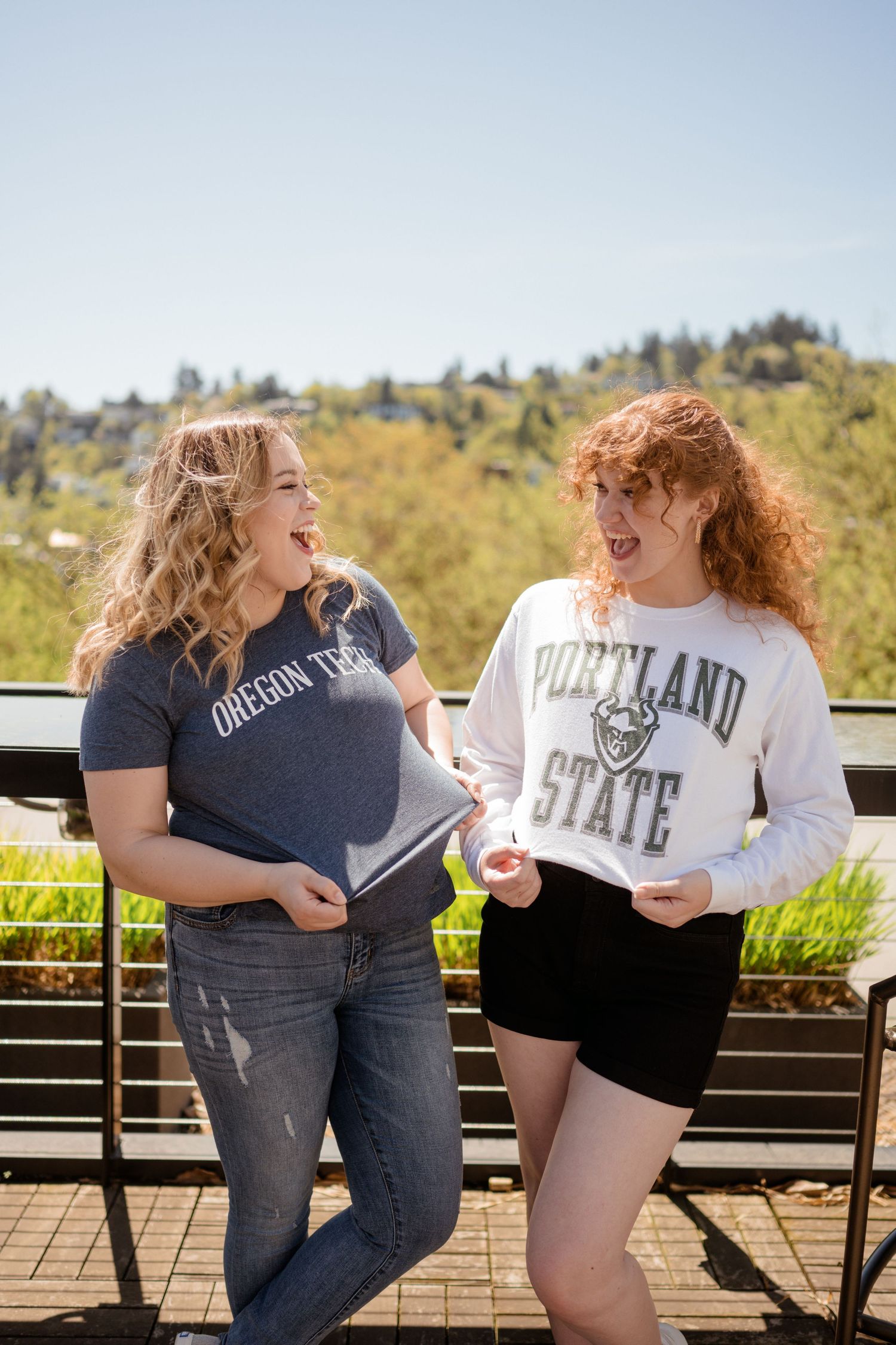 Students wearing university shirts laugh together on outdoor deck.