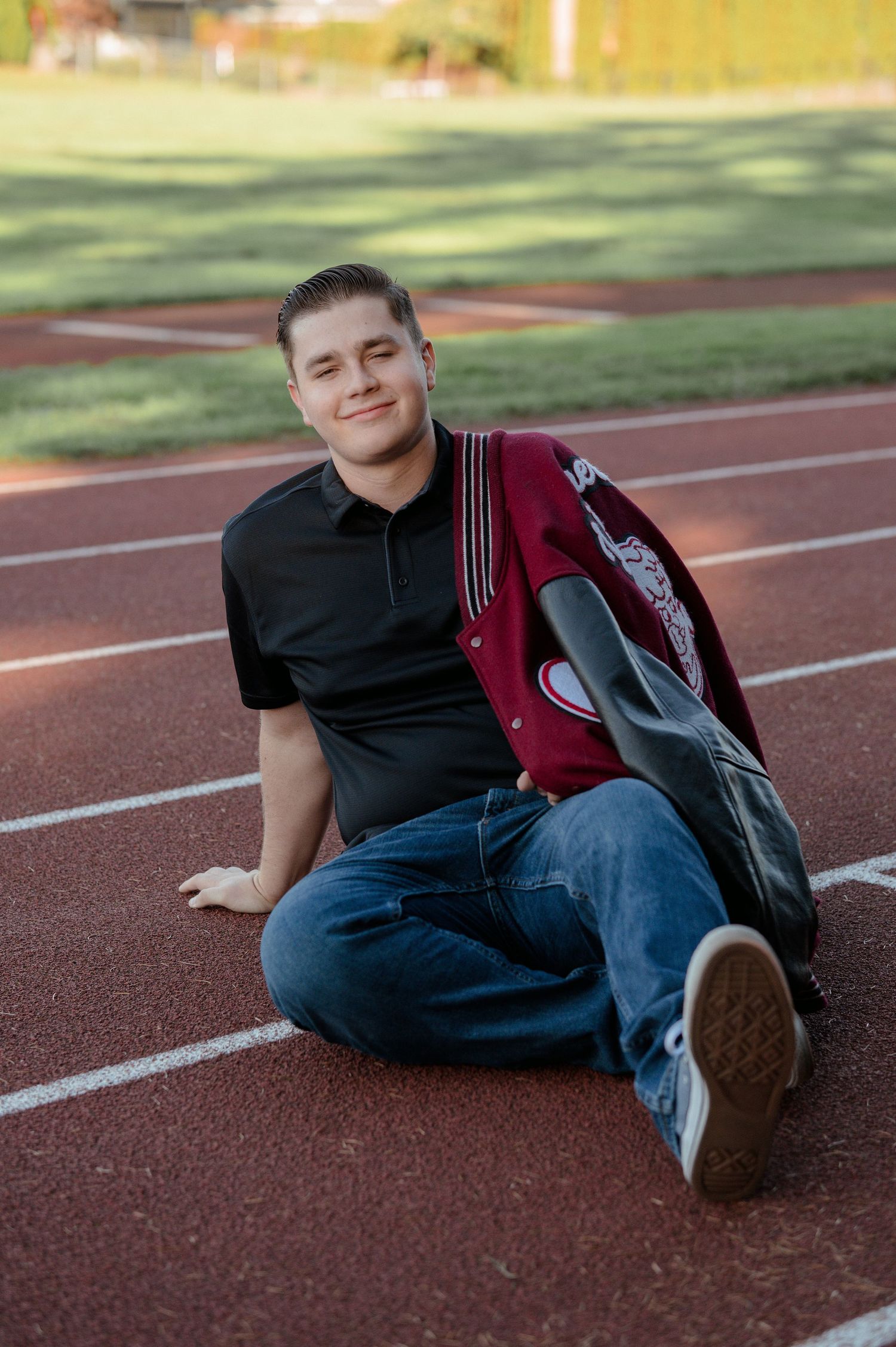 Student sitting on running track with red backpack on sunny day.
