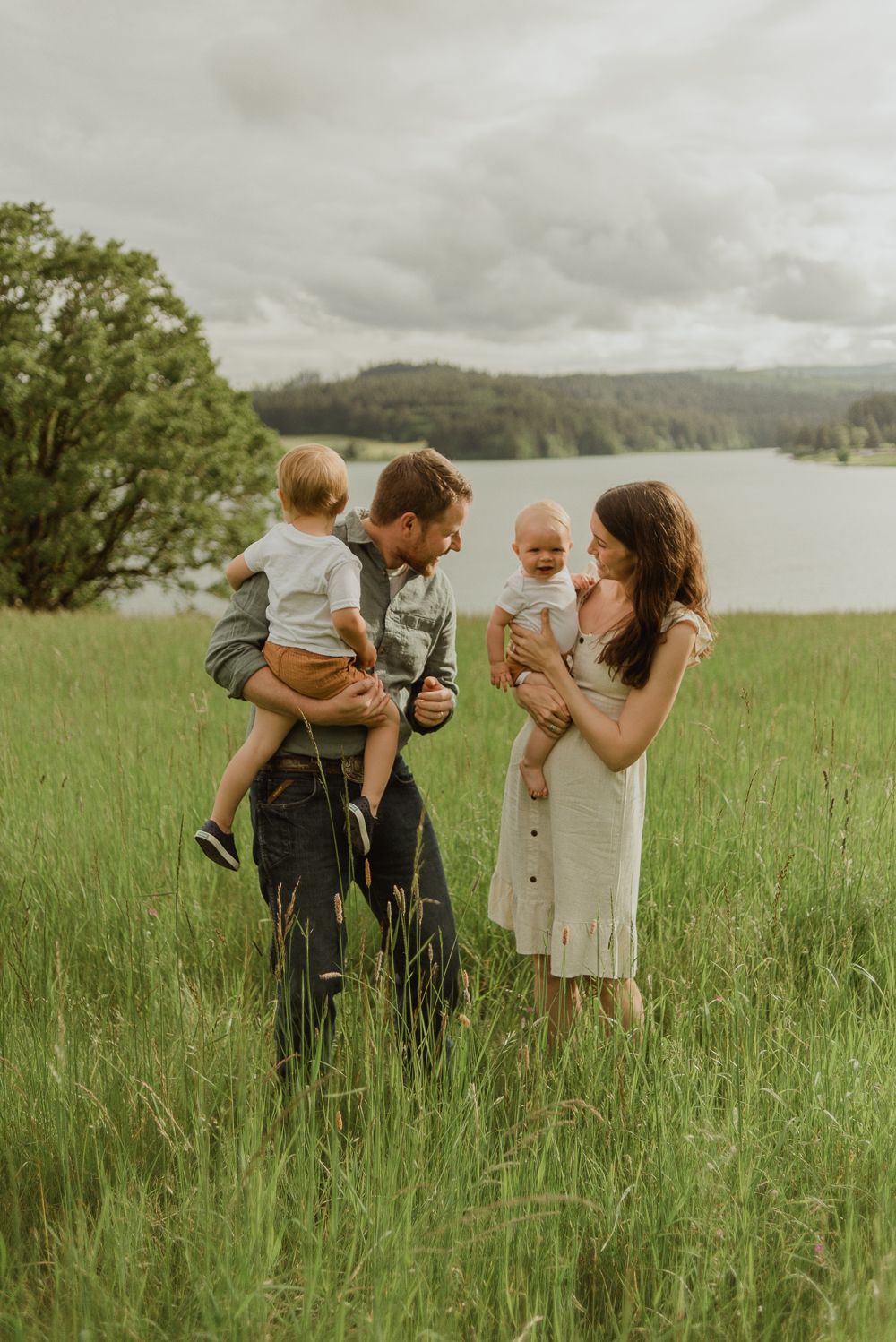 Family sharing tender moment together in green meadow by lakeside on cloudy day.