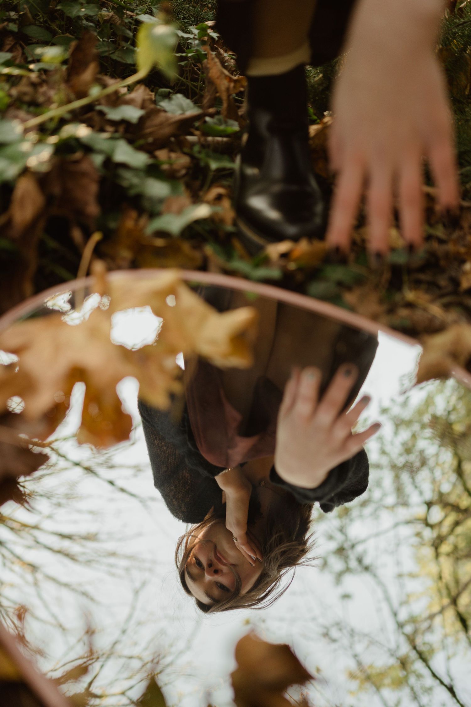 Creative mirror reflection portrait in autumn forest setting with fallen leaves.
