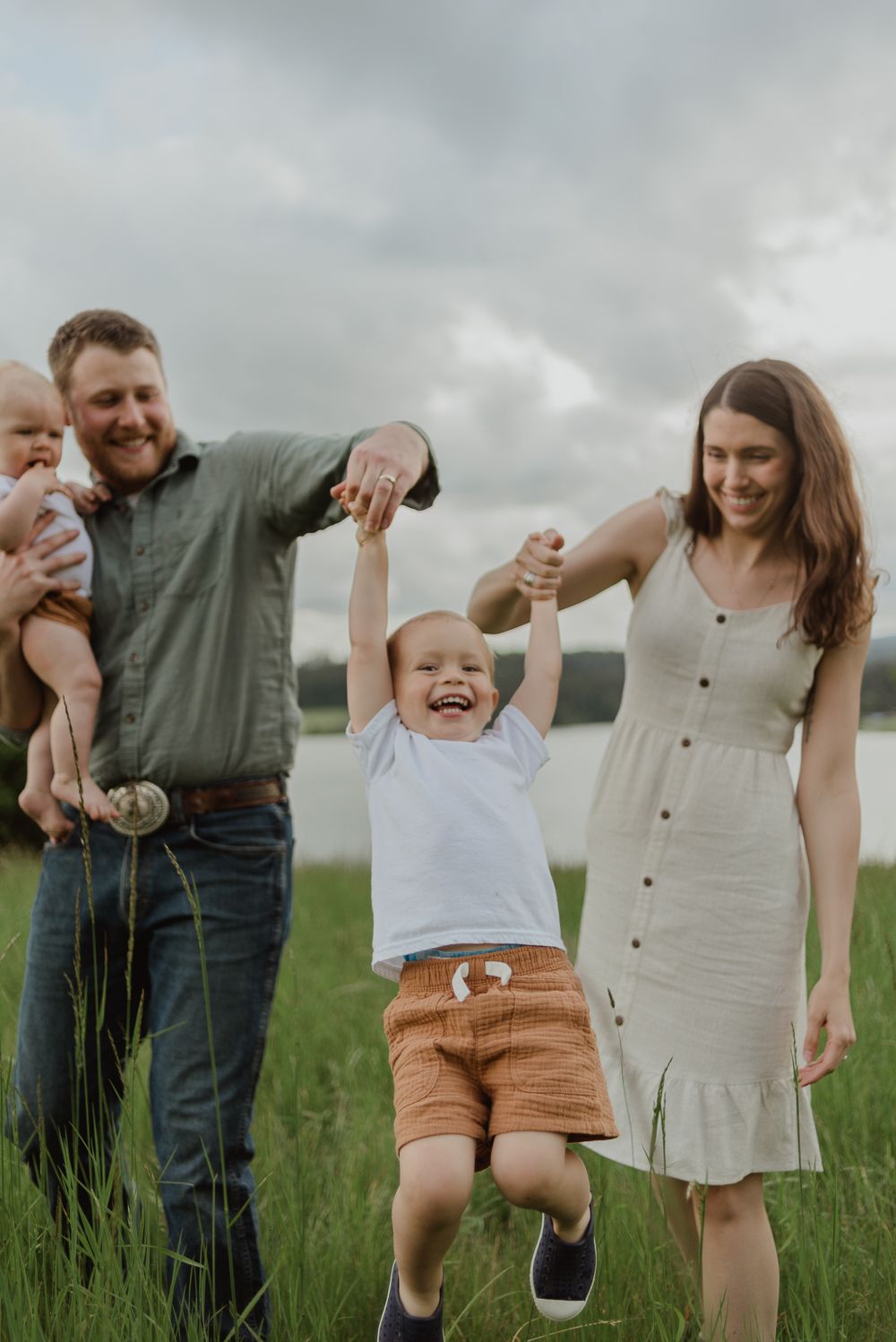Playful family moment in green meadow with lake in background.