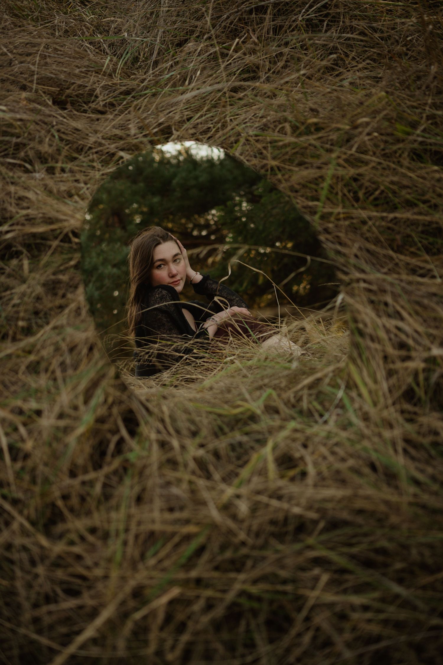 Creative circular mirror portrait framed by dried grass and natural elements.