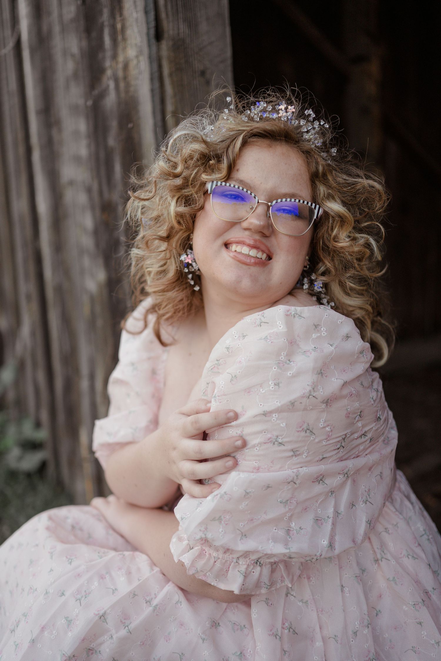 Joyful portrait wearing purple glasses and pink dress against wooden backdrop.