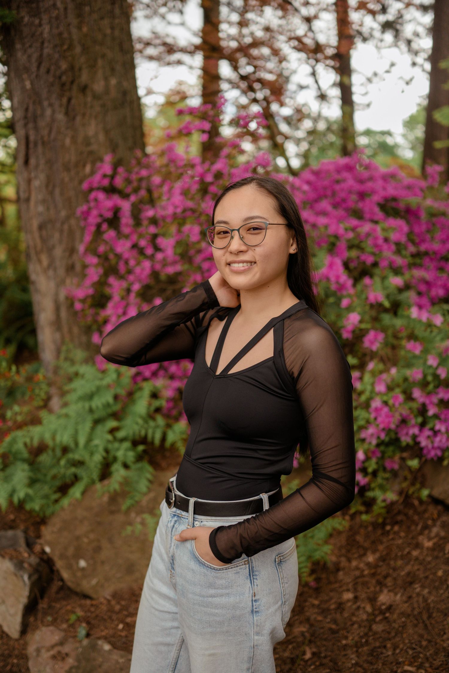 Stylish portrait featuring black mesh top and light denim against pink flowering bushes.