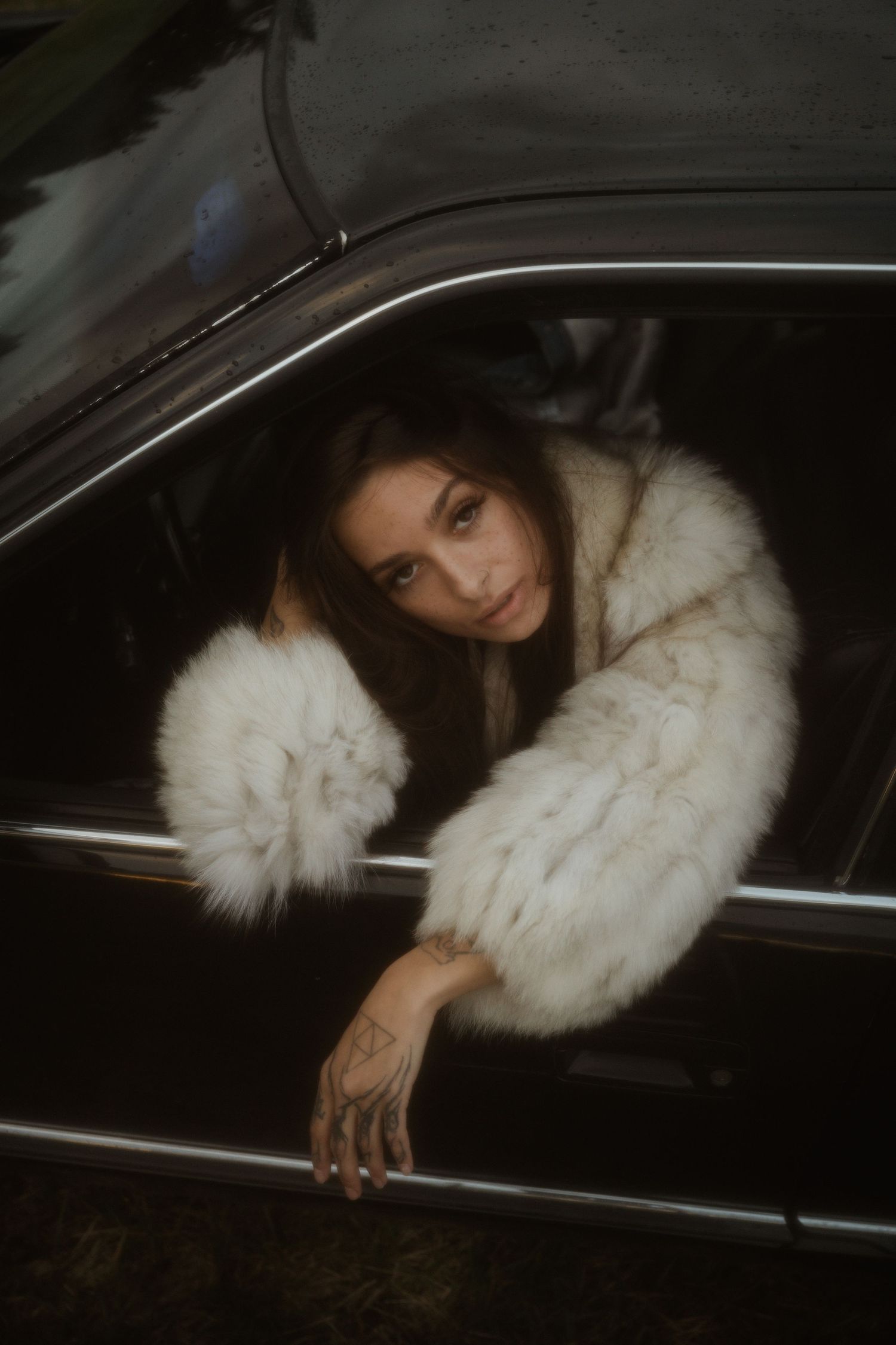 A plush white fur coat peeks out from the window of a sleek dark car at night.