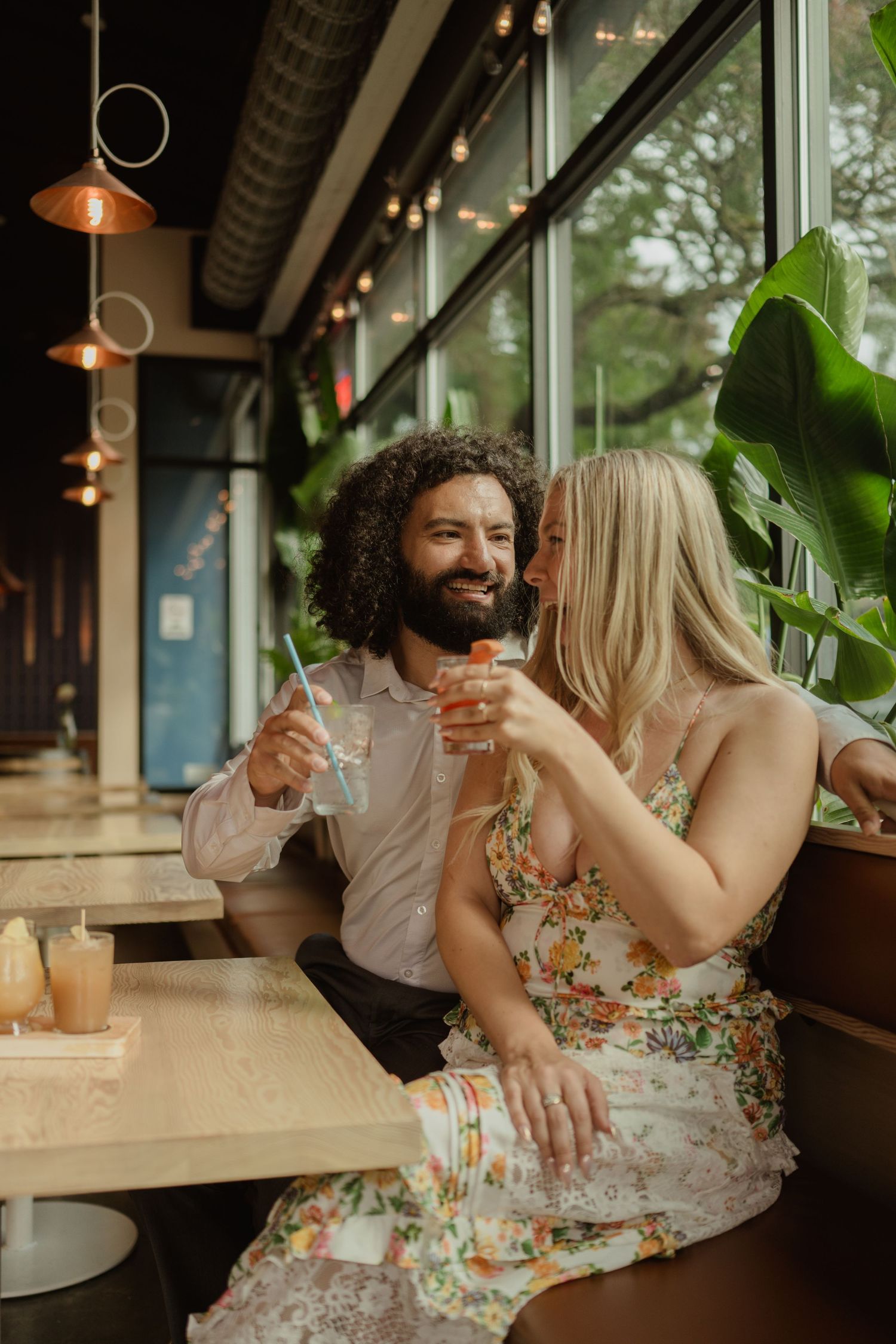 A couple shares drinks and laughter at a cozy restaurant with pendant lighting.