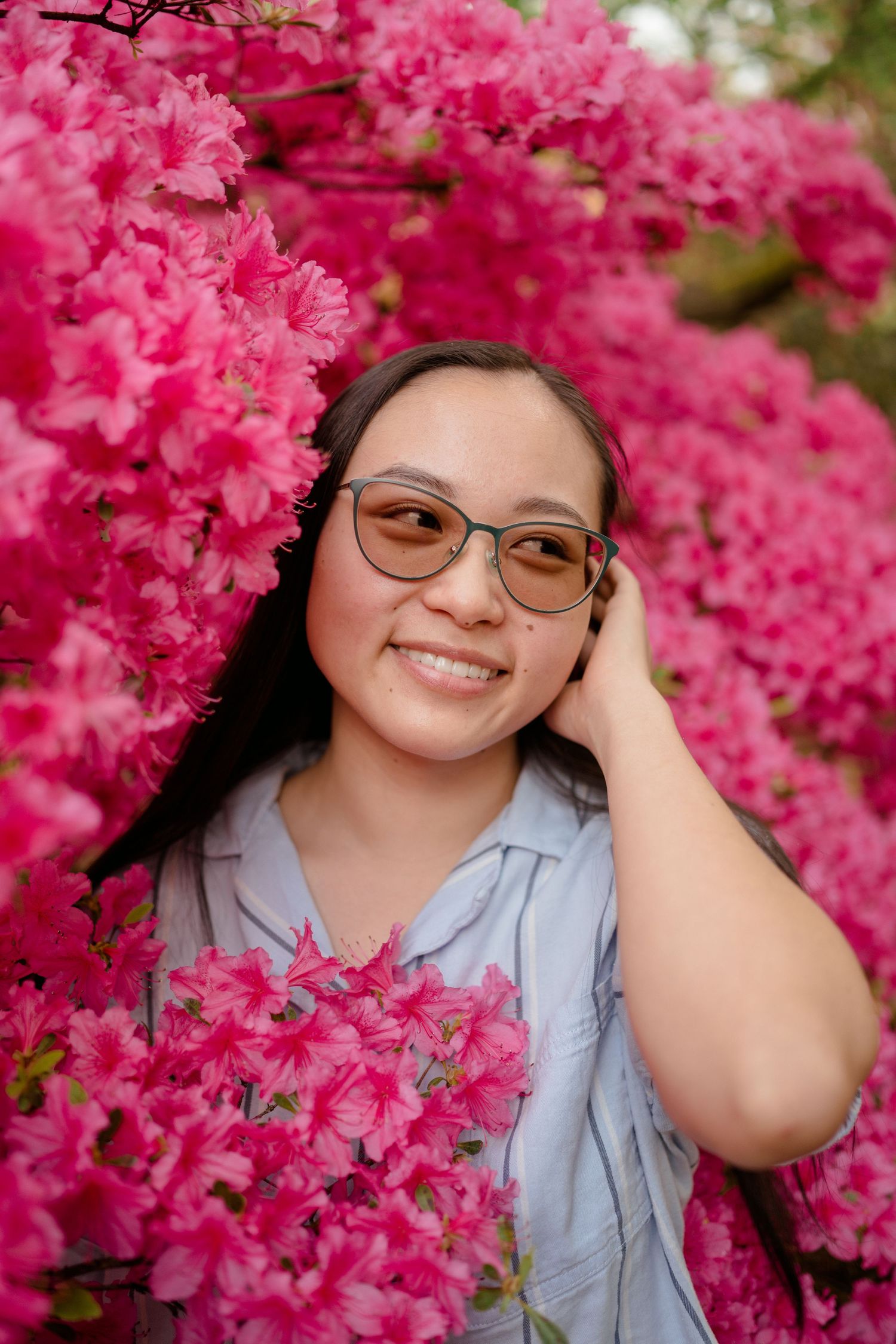Portrait against vibrant pink azalea blossoms wearing glasses and a blue button-up shirt.