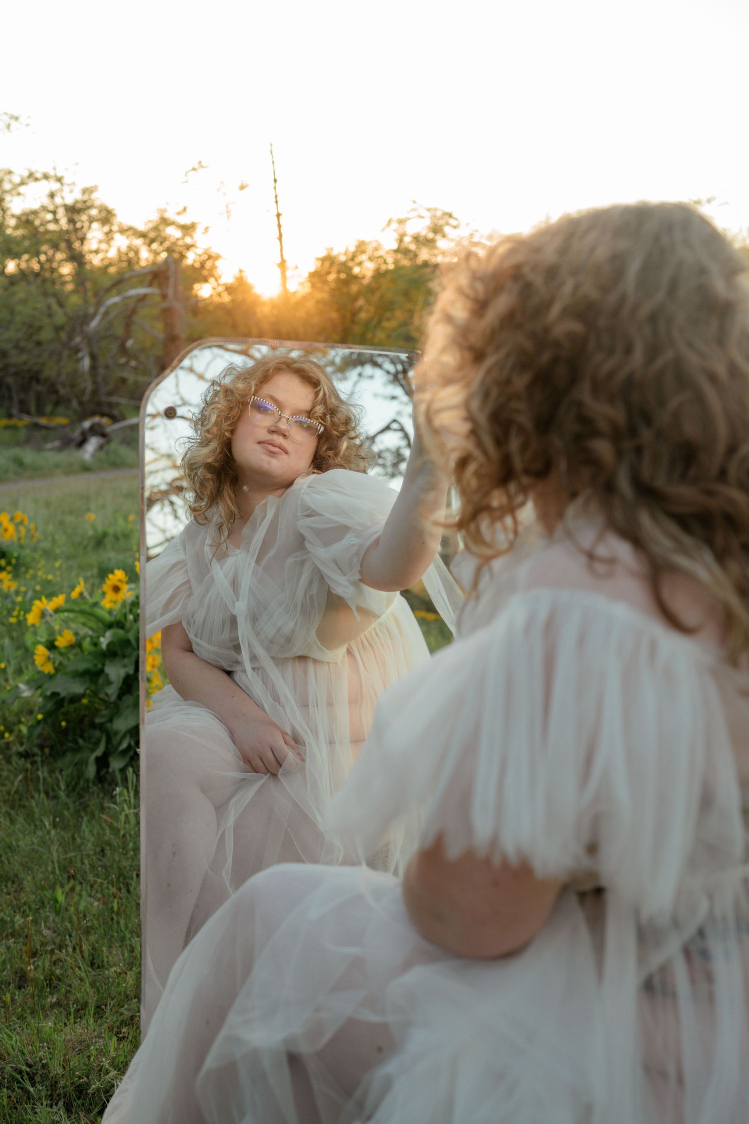 Ethereal outdoor portrait with mirror reflection in field of yellow flowers at sunset.