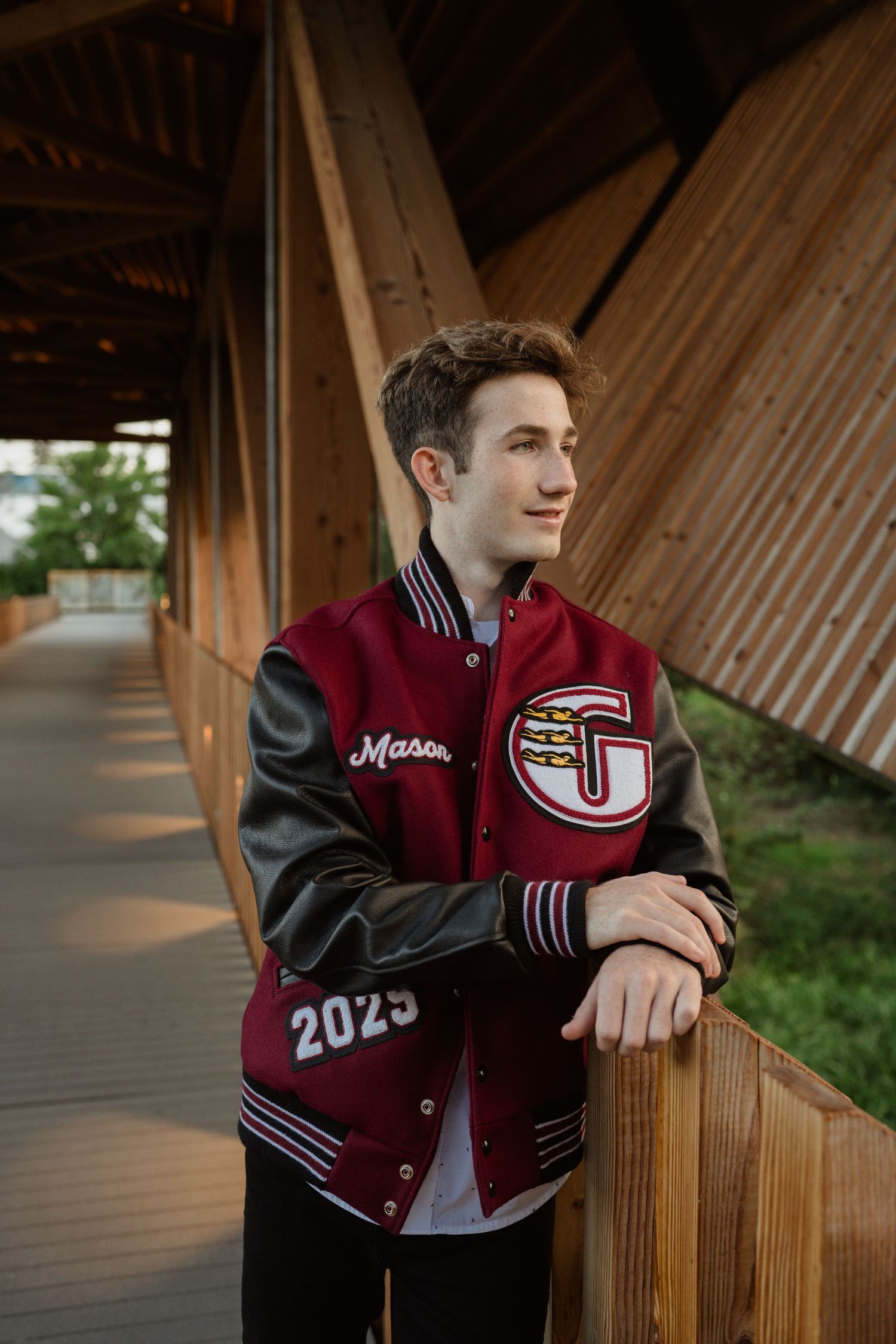 Person in maroon and black varsity jacket poses along wooden walkway.