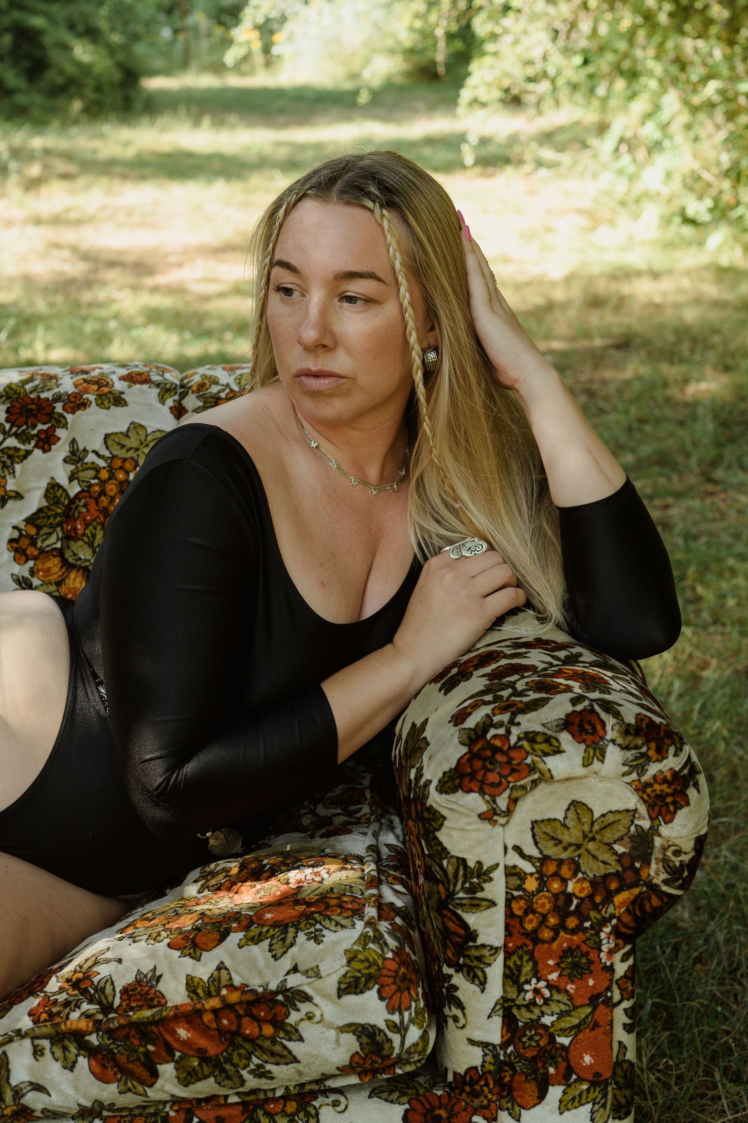 A relaxed outdoor portrait on a floral patterned couch in dappled sunlight.
