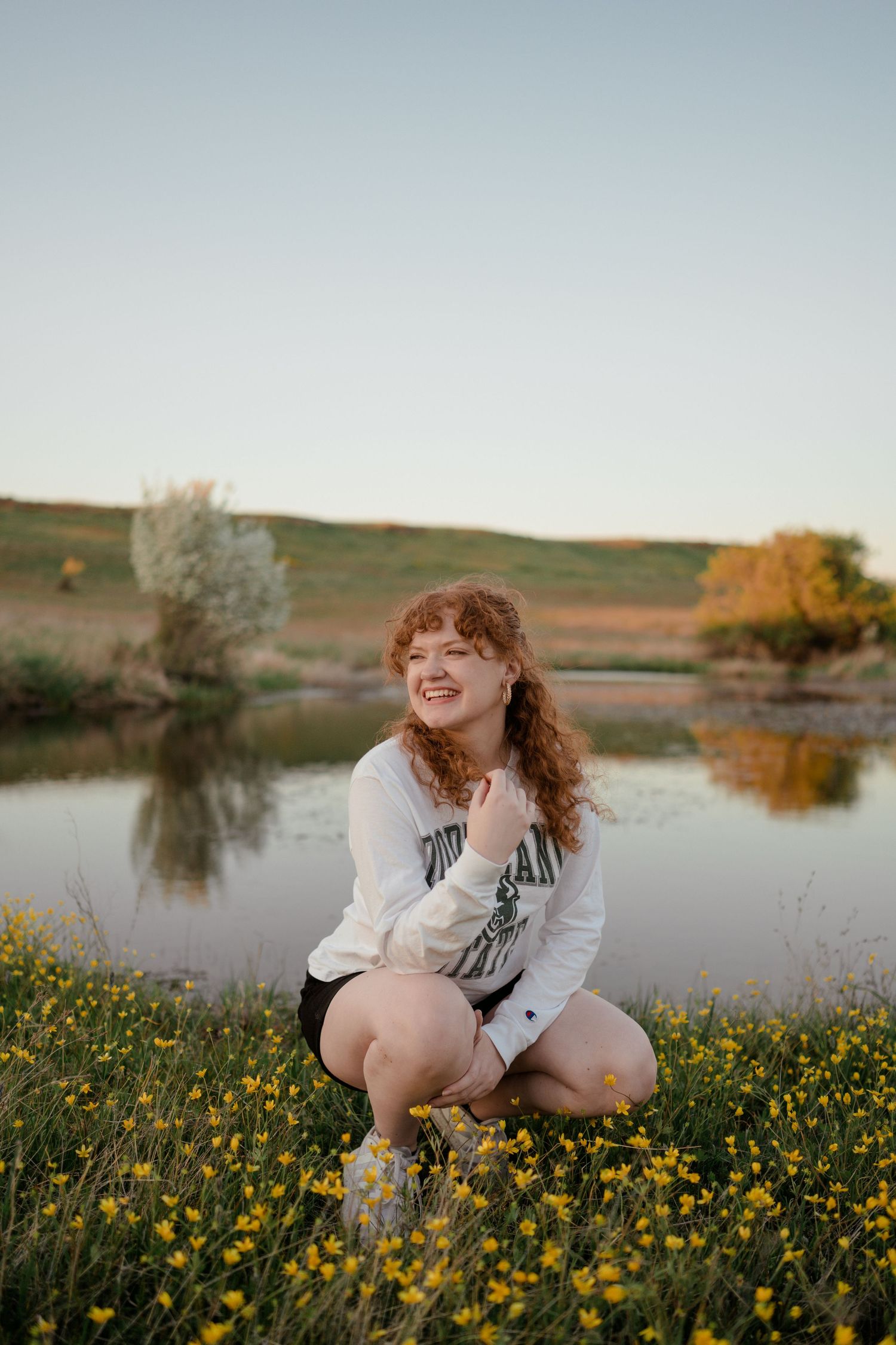 Person sitting among yellow wildflowers by lake at sunset.