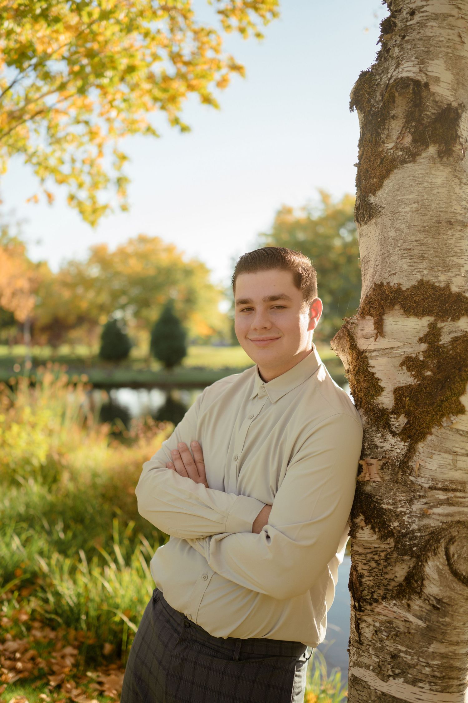 Person in cream sweater standing by birch tree in autumn park setting.