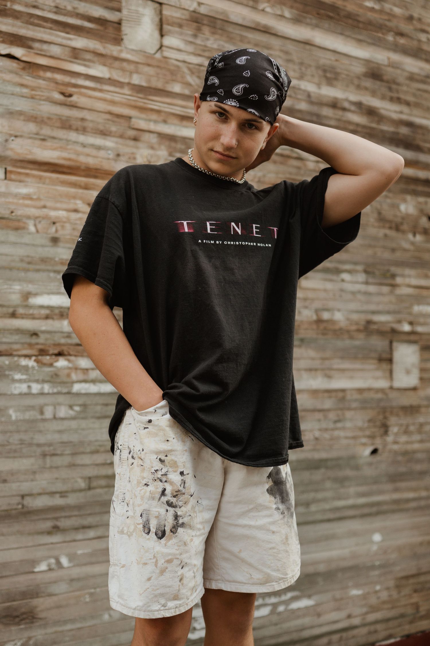 Person wearing TENET t-shirt and bandana poses against wooden wall.