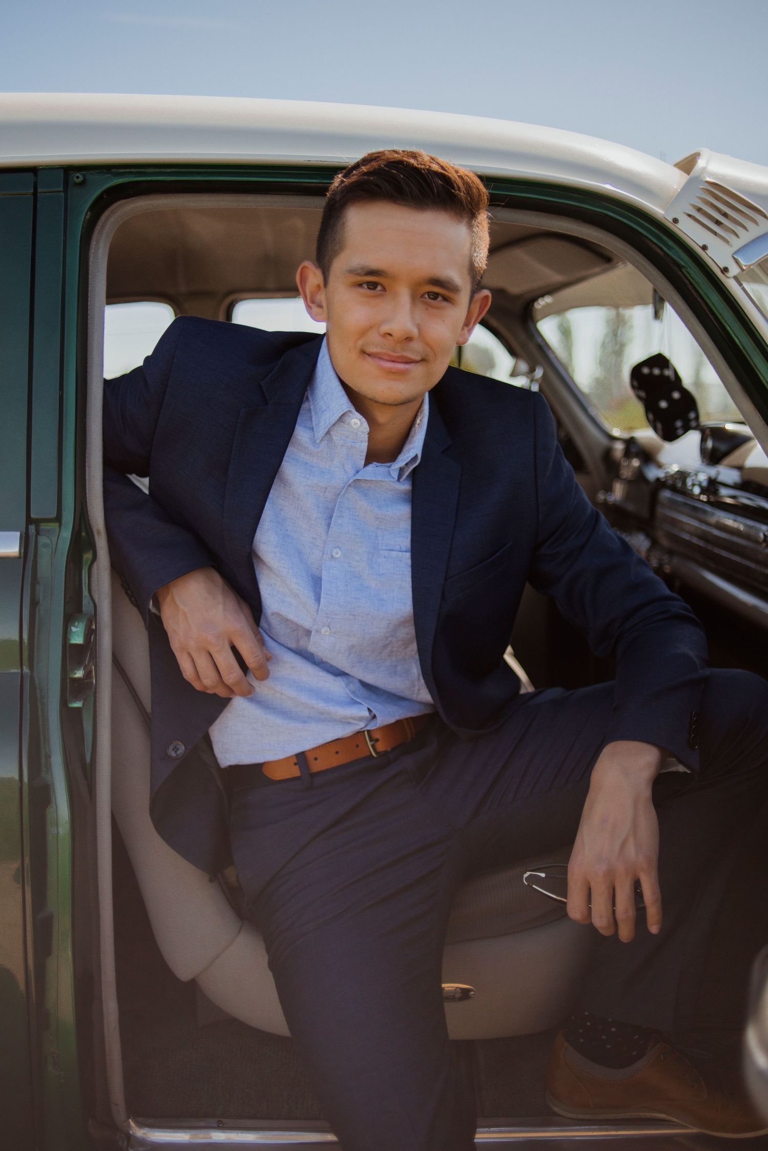 Well-dressed person in navy suit sitting in vintage car doorway.