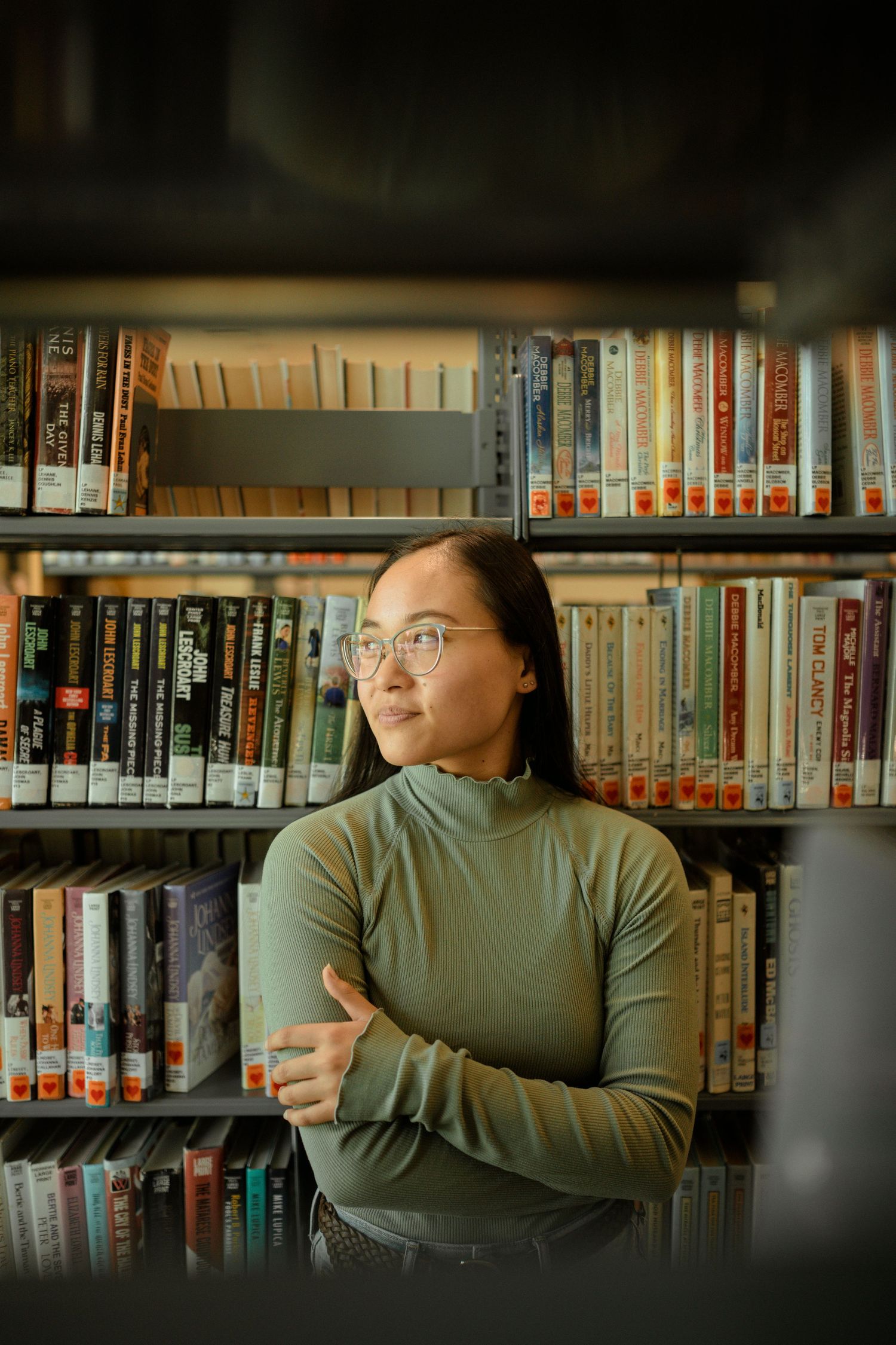 Person in turtleneck sweater standing in front of library shelves filled with books.