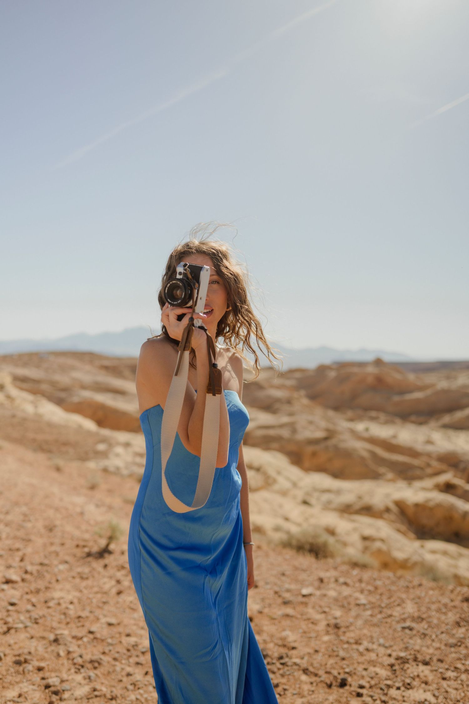 Person in flowing blue dress photographs desert landscape on sunny day.