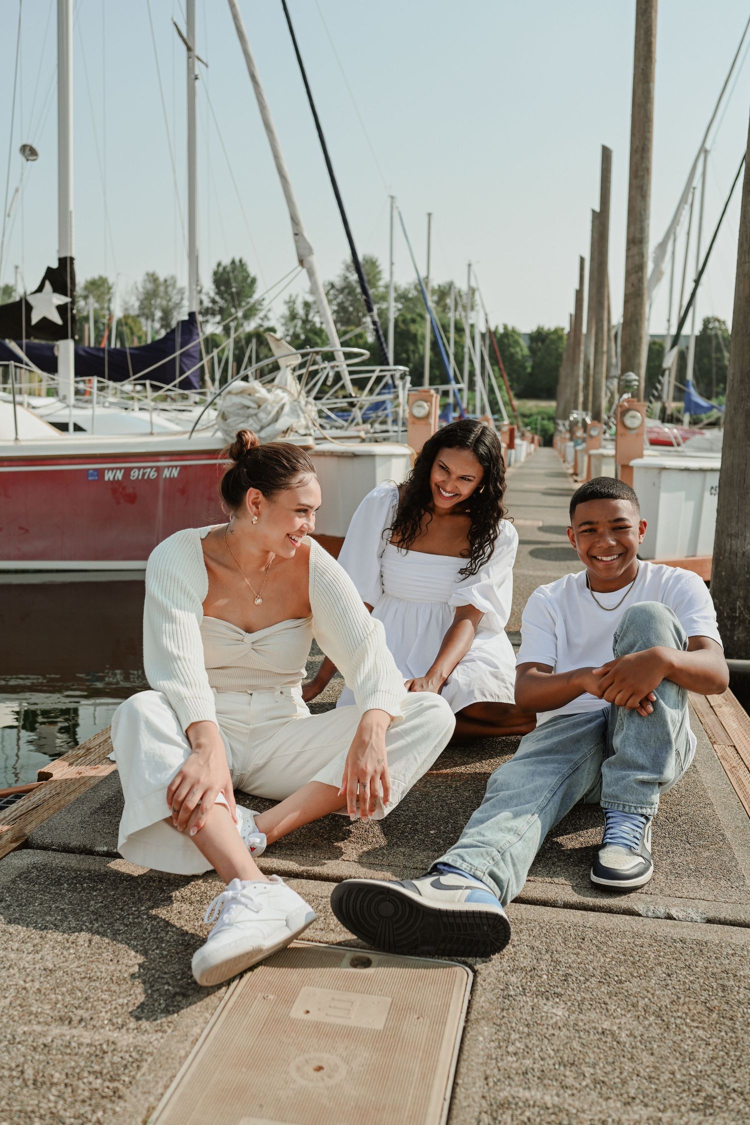 Friends relaxing on dock with sailboats in marina background.