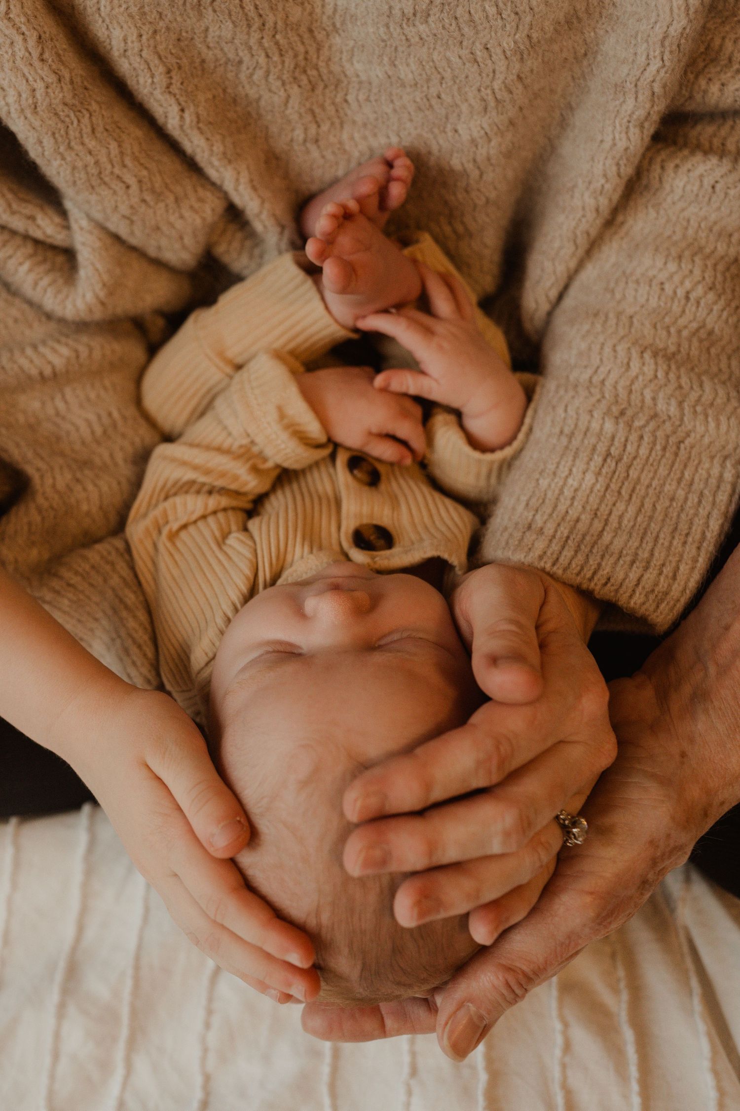 Gentle hands cradling a sleeping newborn in warm knit clothing.