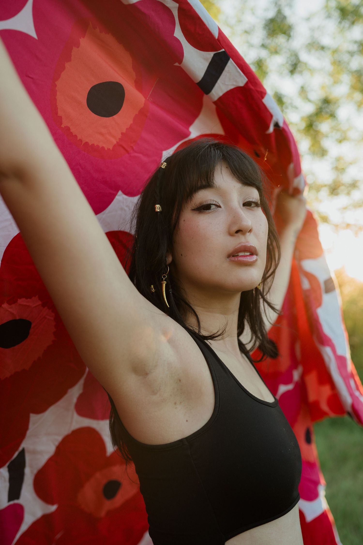Figure in black top poses with red floral Marimekko-style fabric in sunlit outdoor setting.