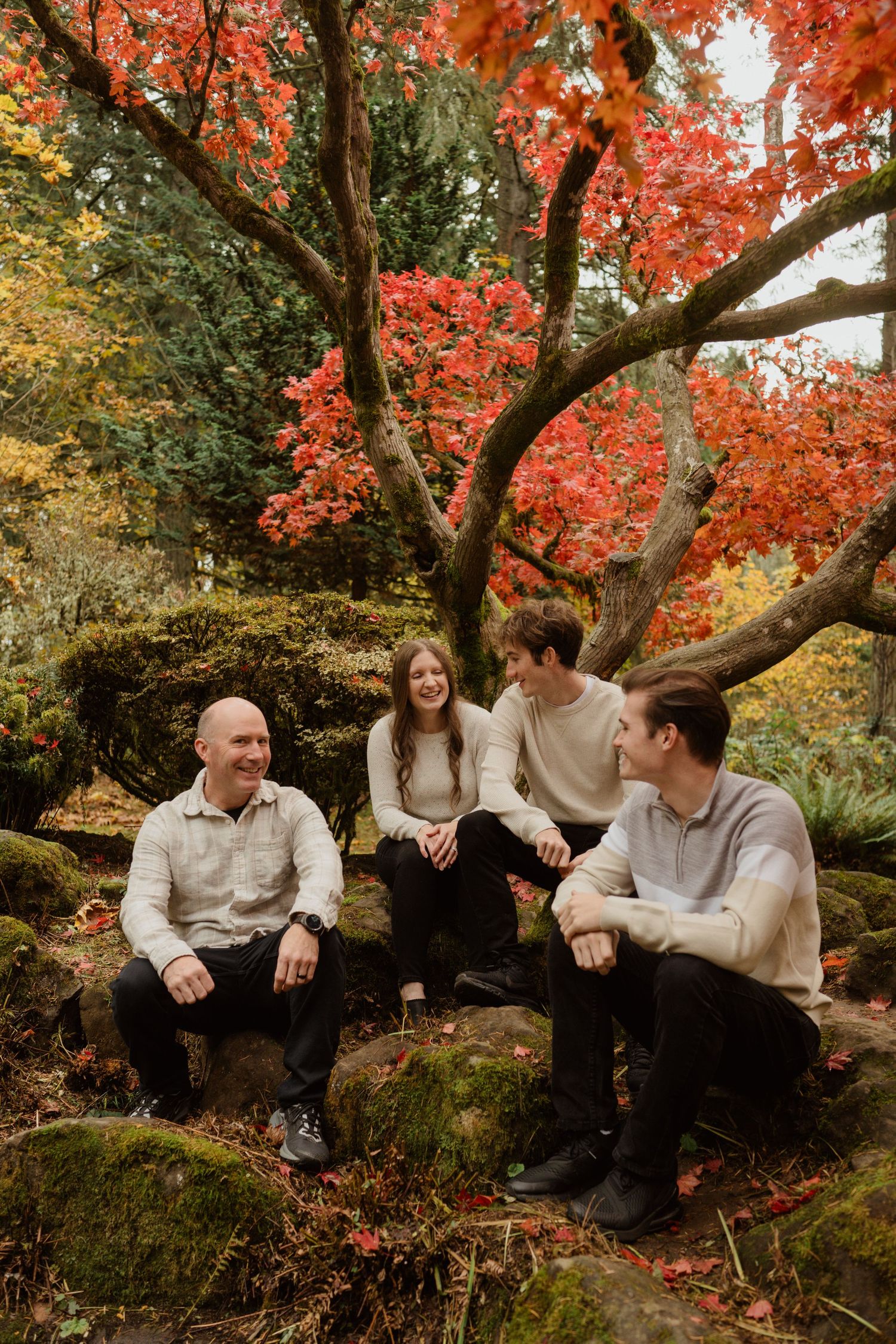 Group sitting on mossy rocks under vibrant red maple trees in autumn.
