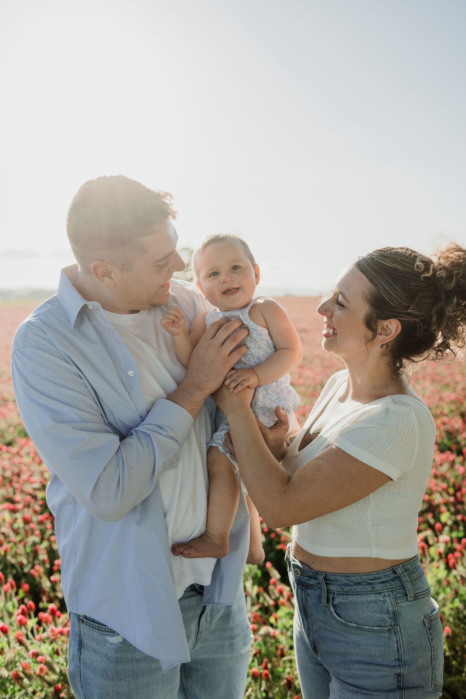 Family sharing joyful moment in sunny flower field with light blue sky background.
