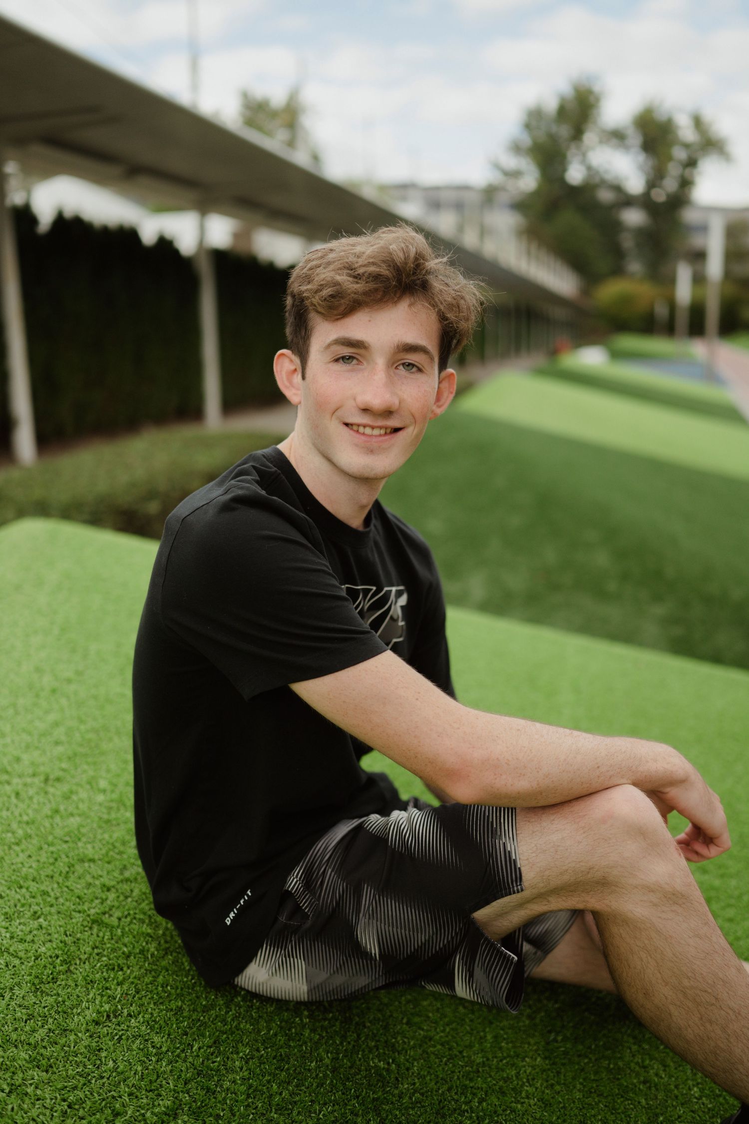 Portrait on artificial turf wearing black t-shirt and shorts in outdoor setting.