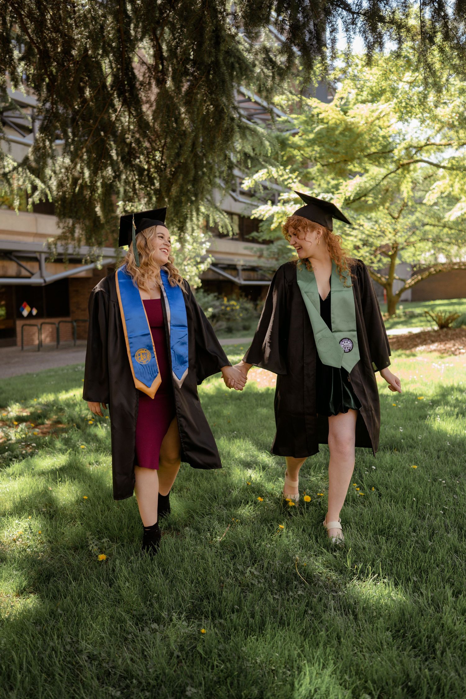 Graduation photo of friends walking on grass path wearing ceremonial caps and gowns.