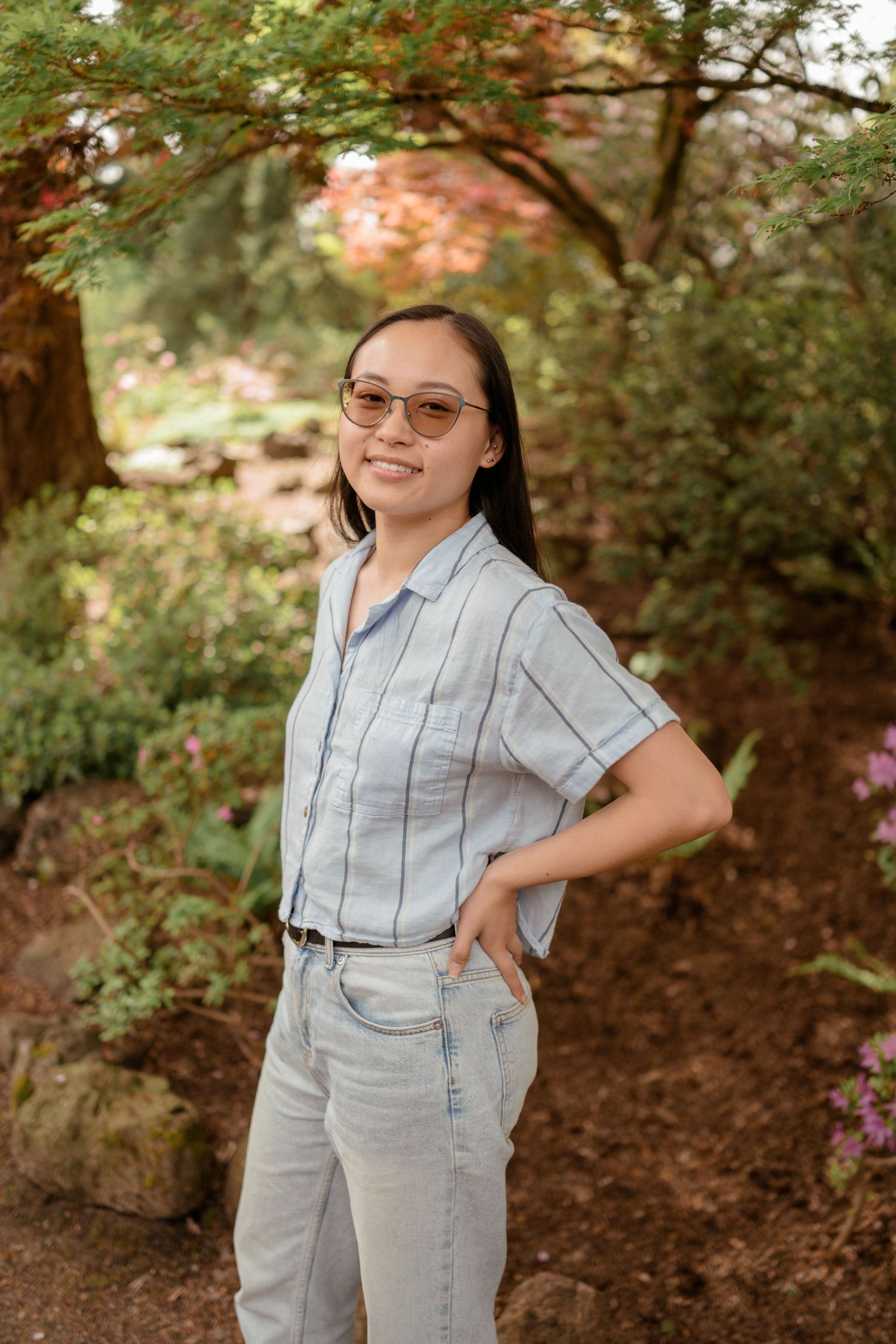Casual outdoor portrait in striped shirt and jeans against autumn foliage background.