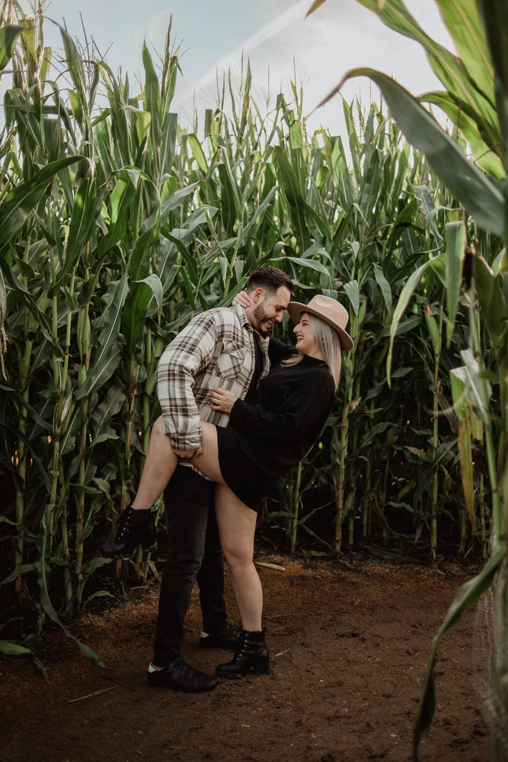 A romantic couple embraces in a cornfield during a photo shoot at sunset.