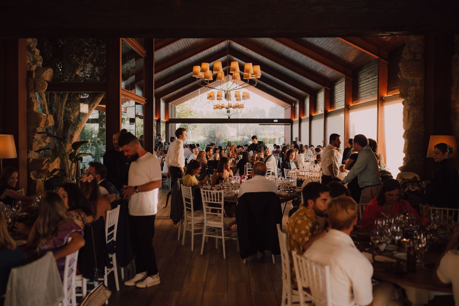 Wedding reception venue filled with tables and guests under vaulted wooden ceiling.