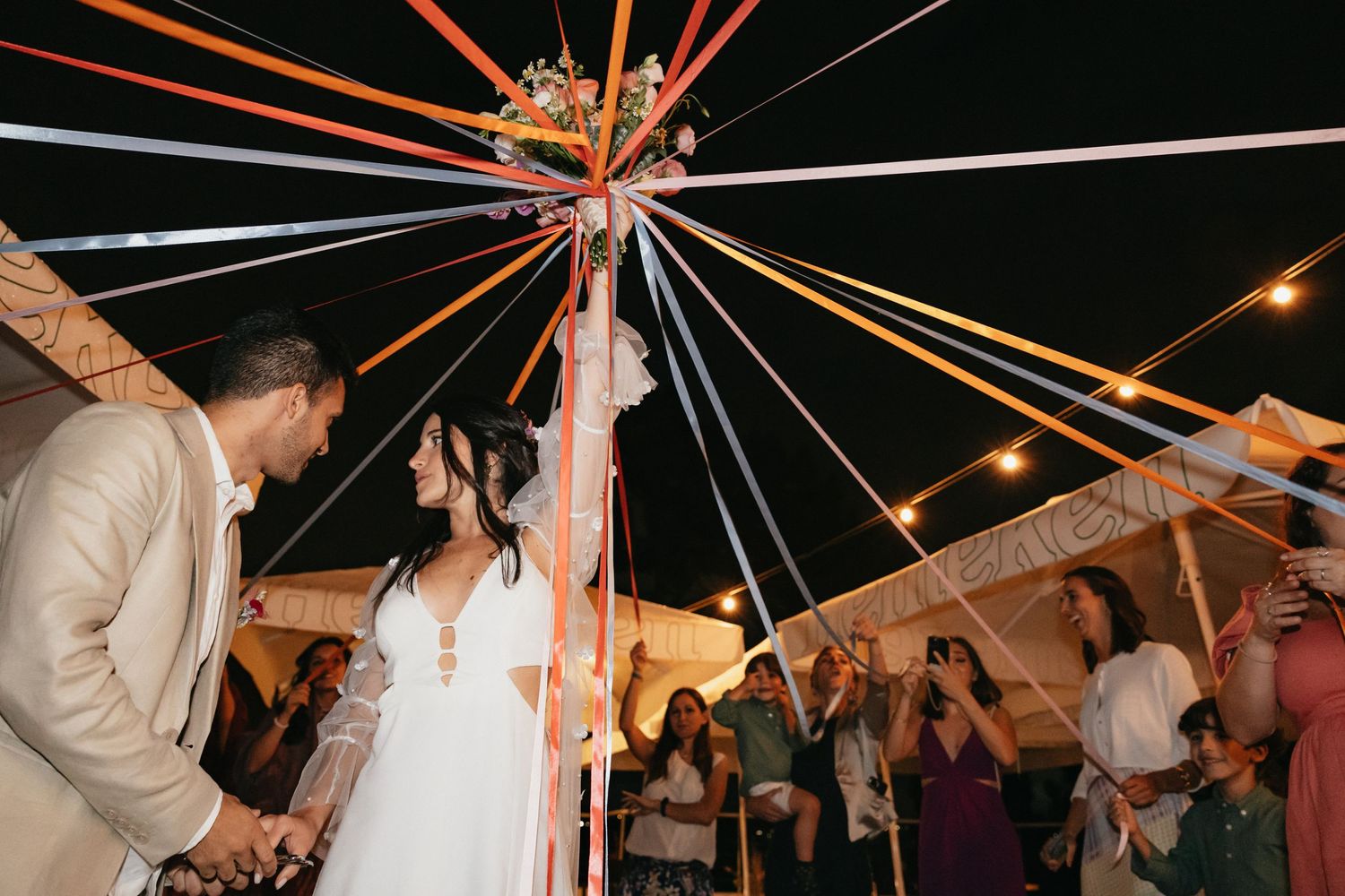 Wedding party celebrating under a star formation of colorful ribbons at night.