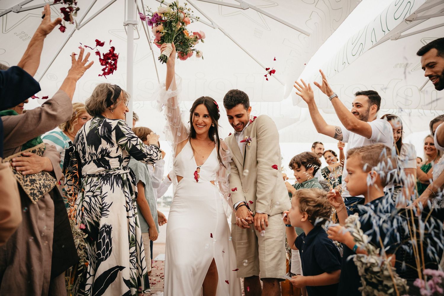 Wedding celebration under a white tent as guests shower the newlyweds with flower petals.