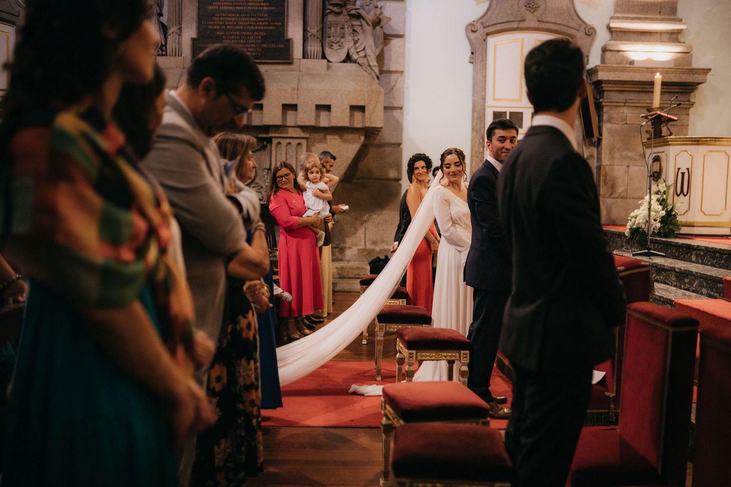 Wedding ceremony in progress on red carpet with attendees watching in historic church setting.