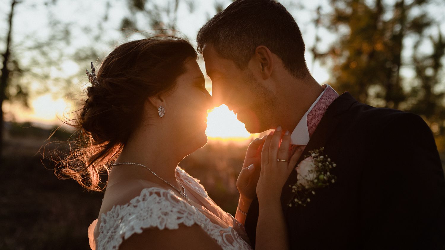 Romantic sunset silhouette of couple in wedding attire with golden sunlight between them.